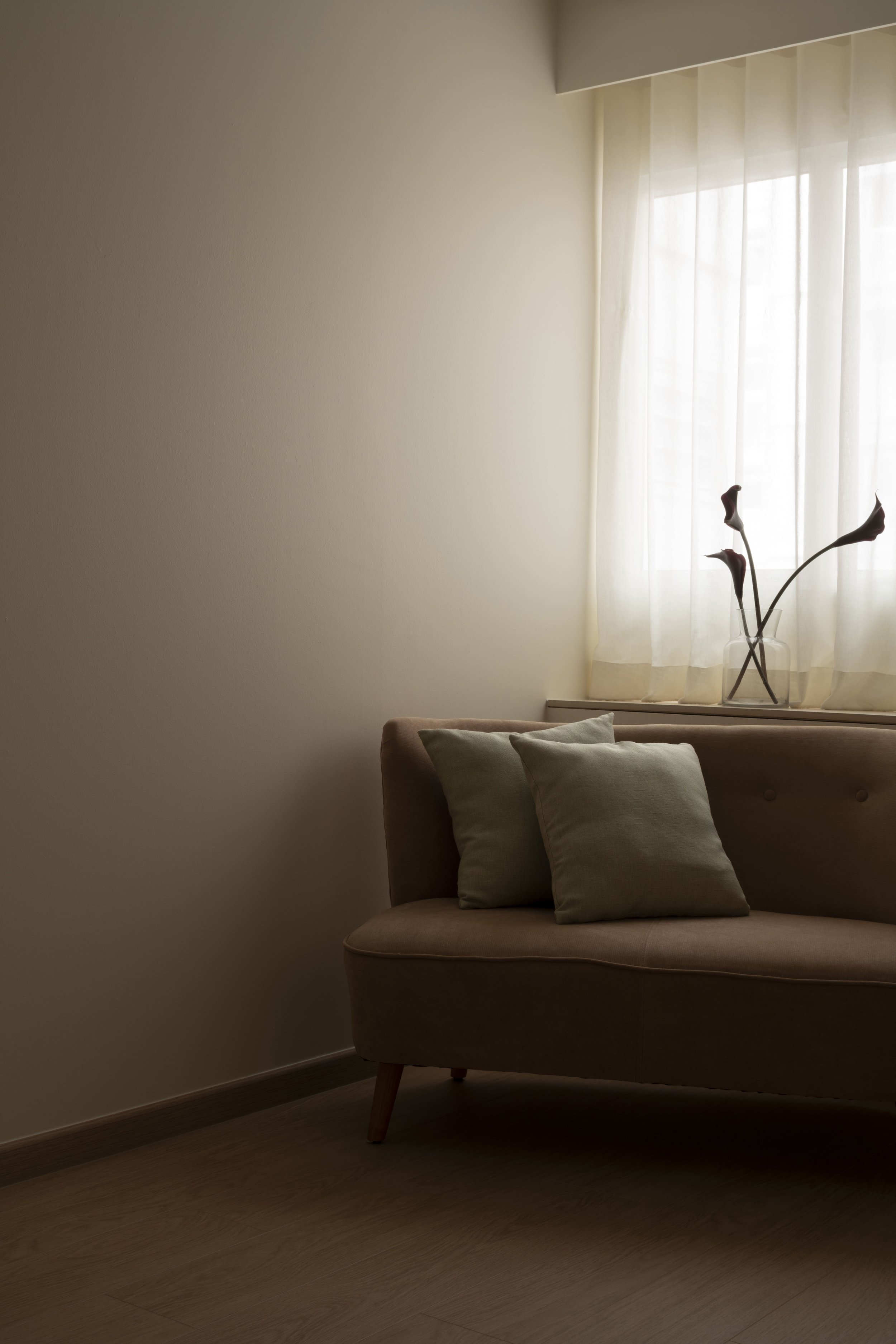 Cozy minimalist bedroom corner with soft natural light, neutral sofa seating, and sheer curtains in a warm modern interior.
