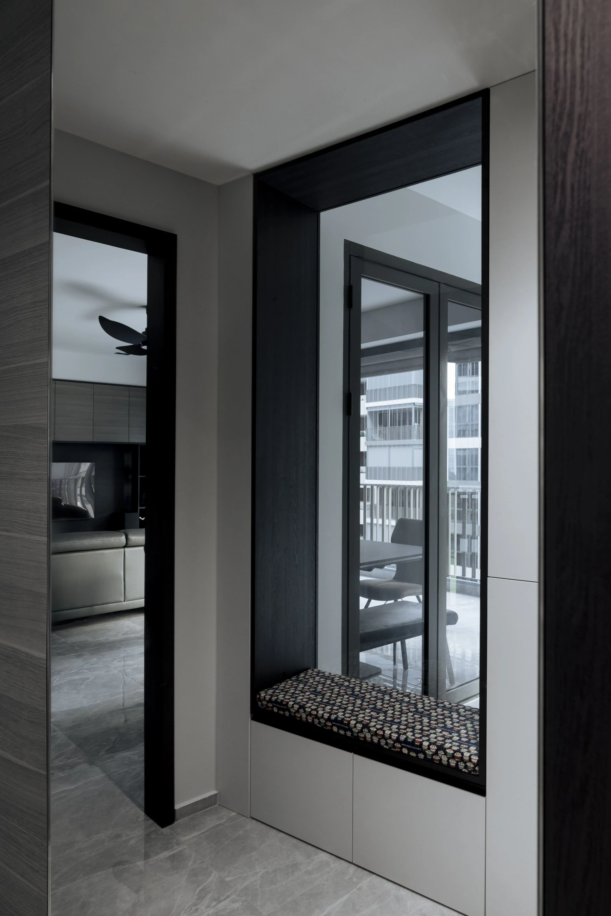 Contemporary entryway design in a Singapore condominium featuring a built-in bench, dark wood framing and reflective mirror panel.