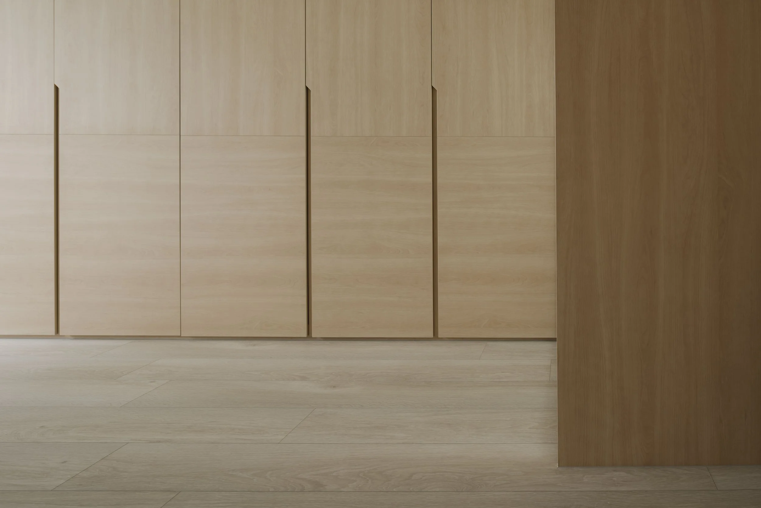Custom light wood floor-to-ceiling wardrobe with clean lines and recessed handles in a minimalist modern walk in wardrobe..