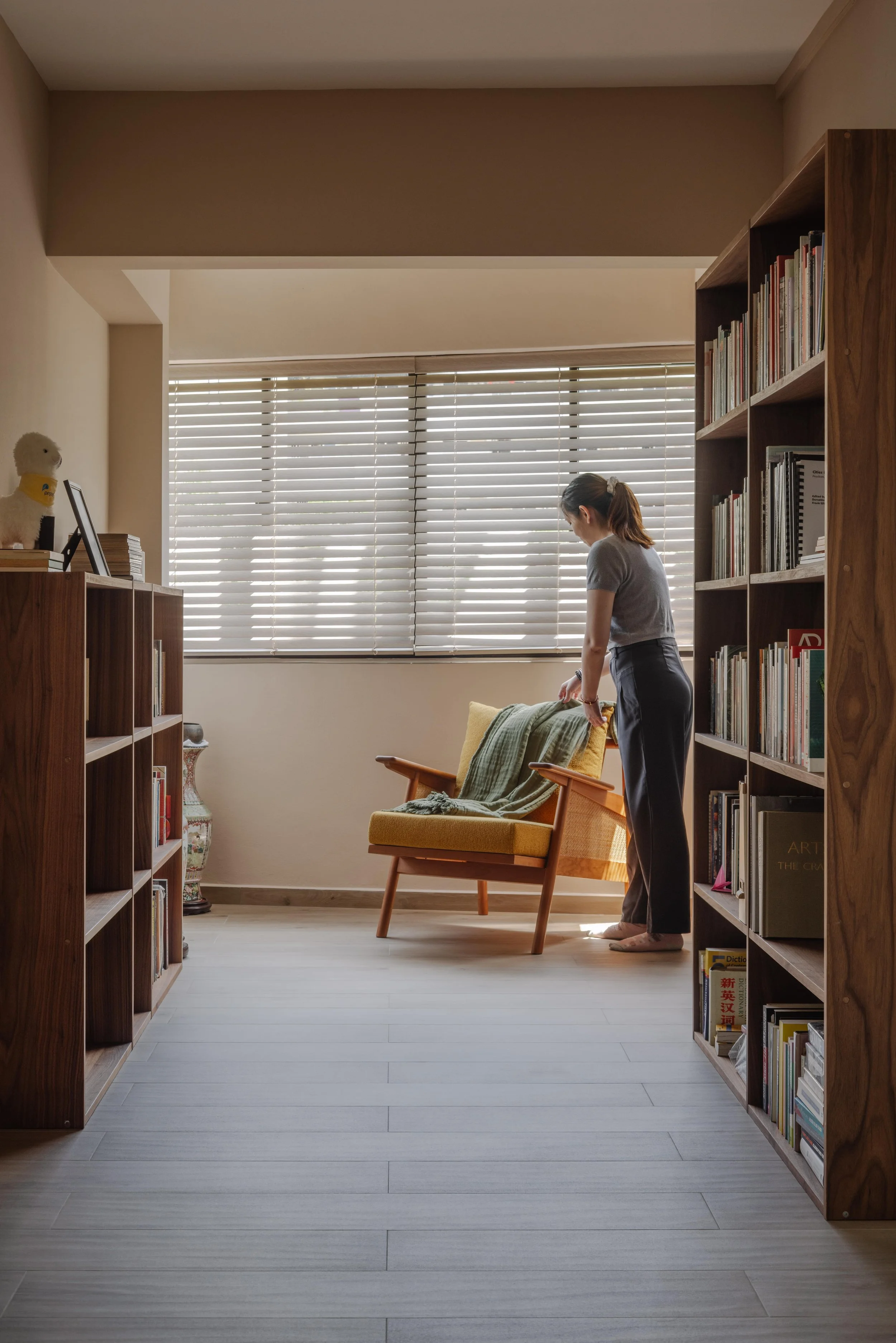 Calm reading nook in a Singapore home featuring timber bookshelves, soft natural light and a mid-century style armchair.