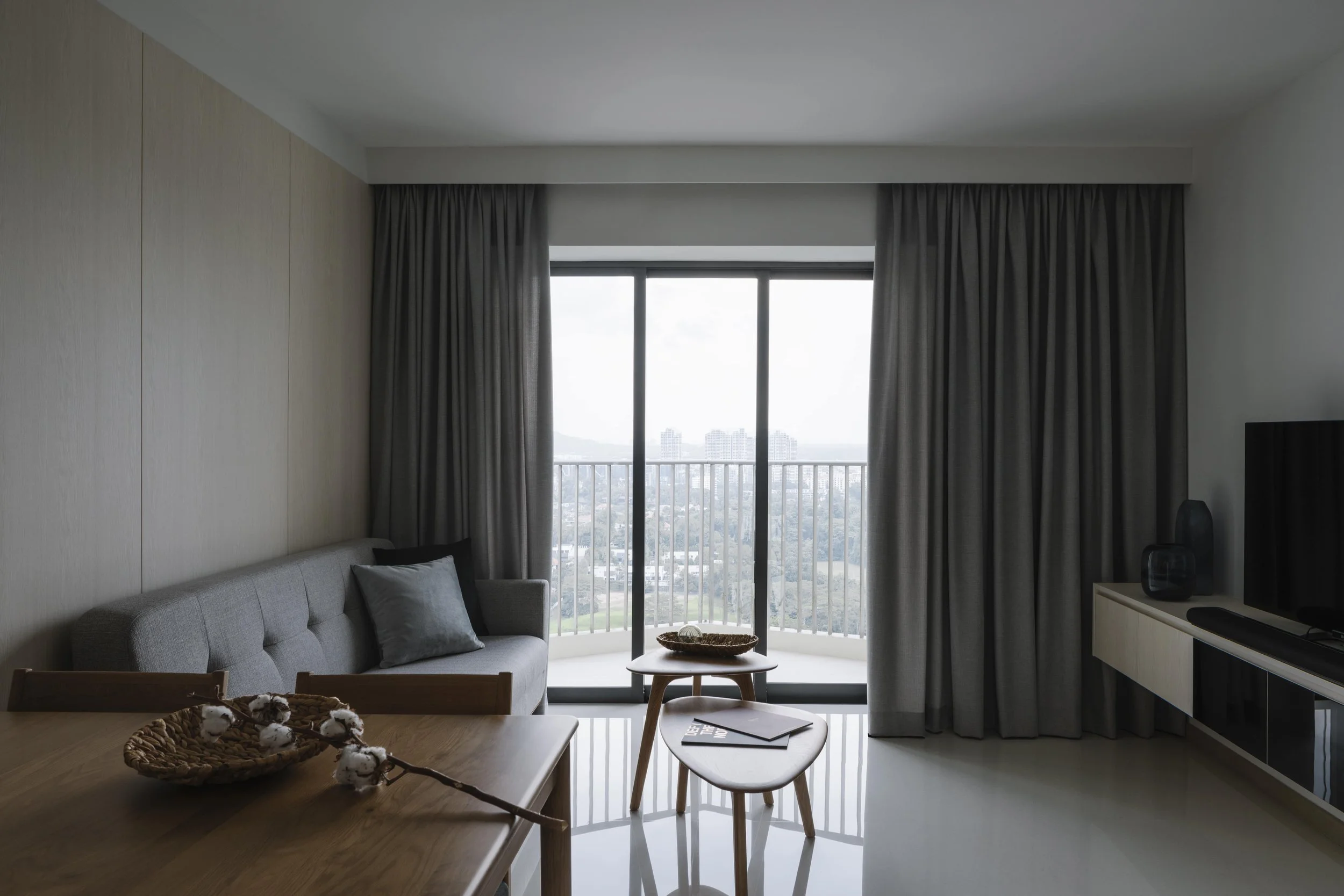 Modern Singapore condo living room with grey sofa, full-height curtains and balcony city view.