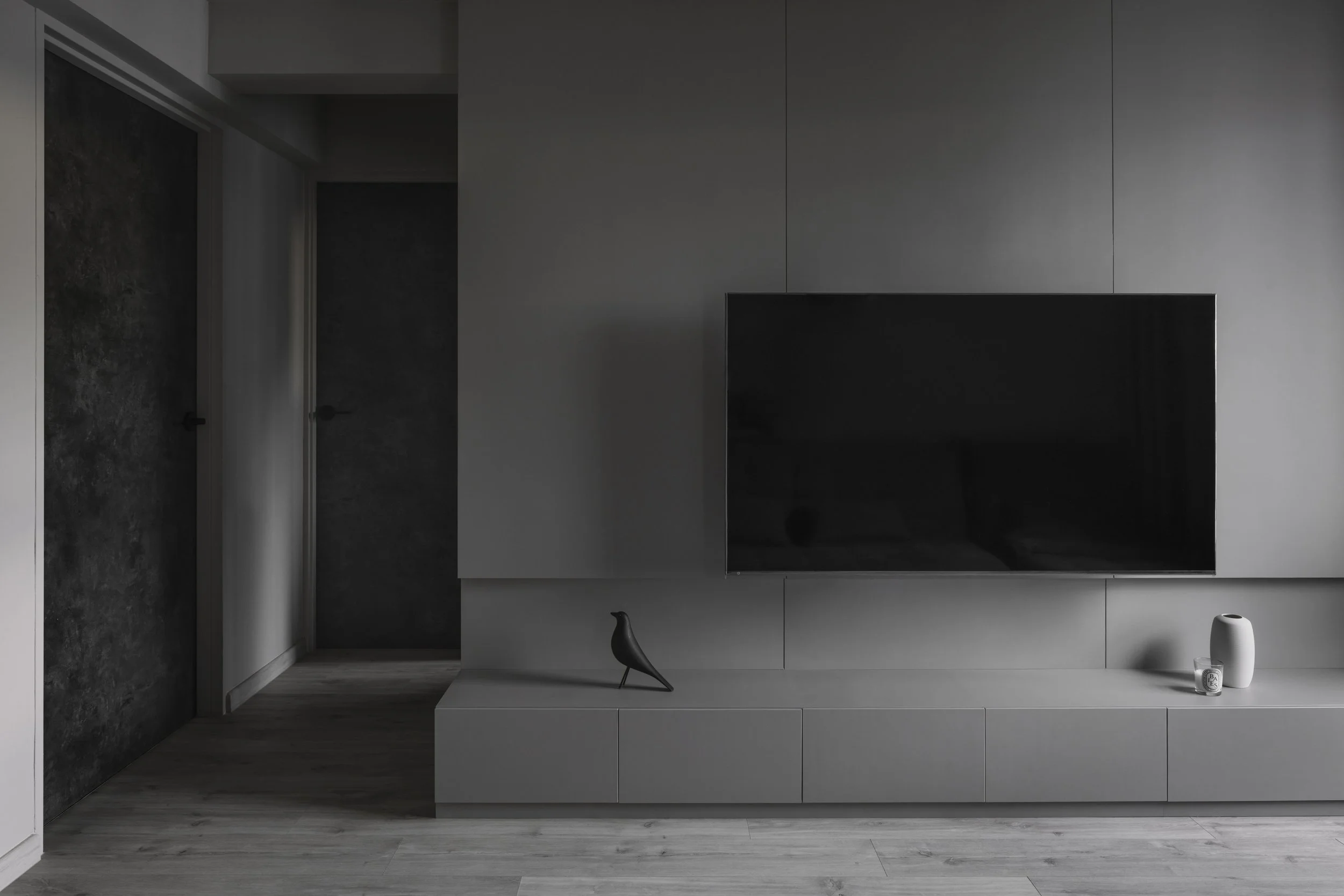 Minimalist grey TV feature wall with built-in console and sculptural décor in a monochromatic living room.