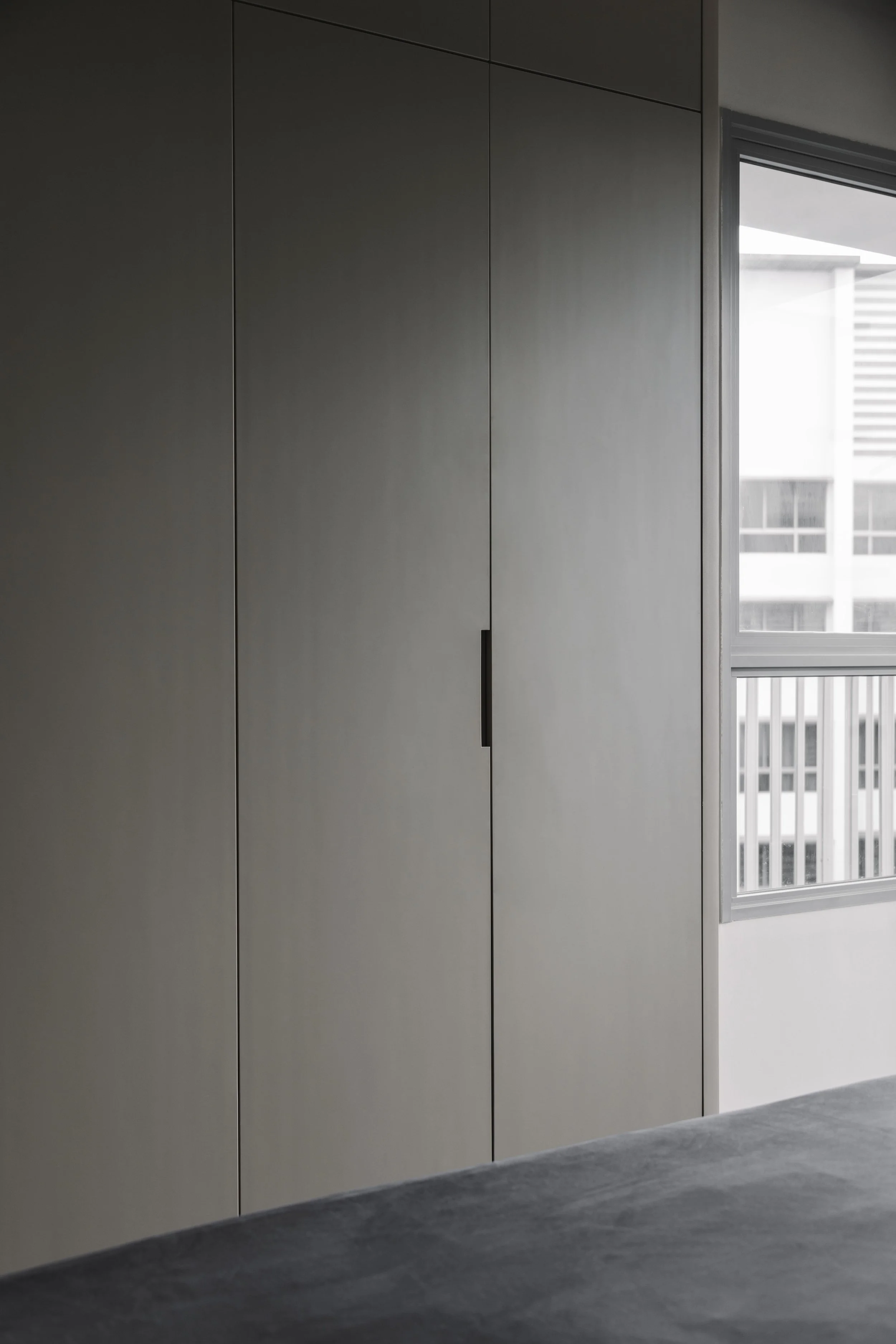 Full-height minimalist wardrobe with matte grey panel doors and integrated handle in a modern bedroom.