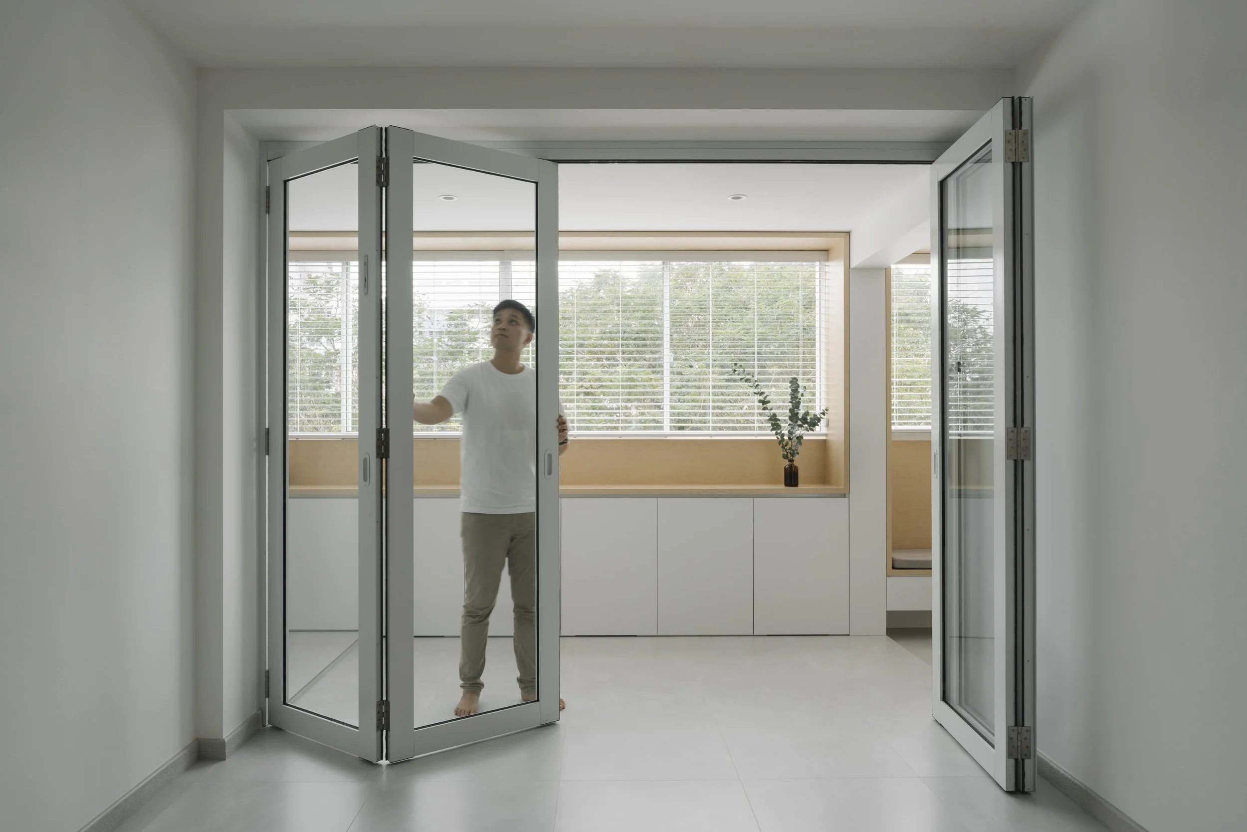 Opening aluminum bi-fold glass doors separating the living area from a light-filled built-in window nook.