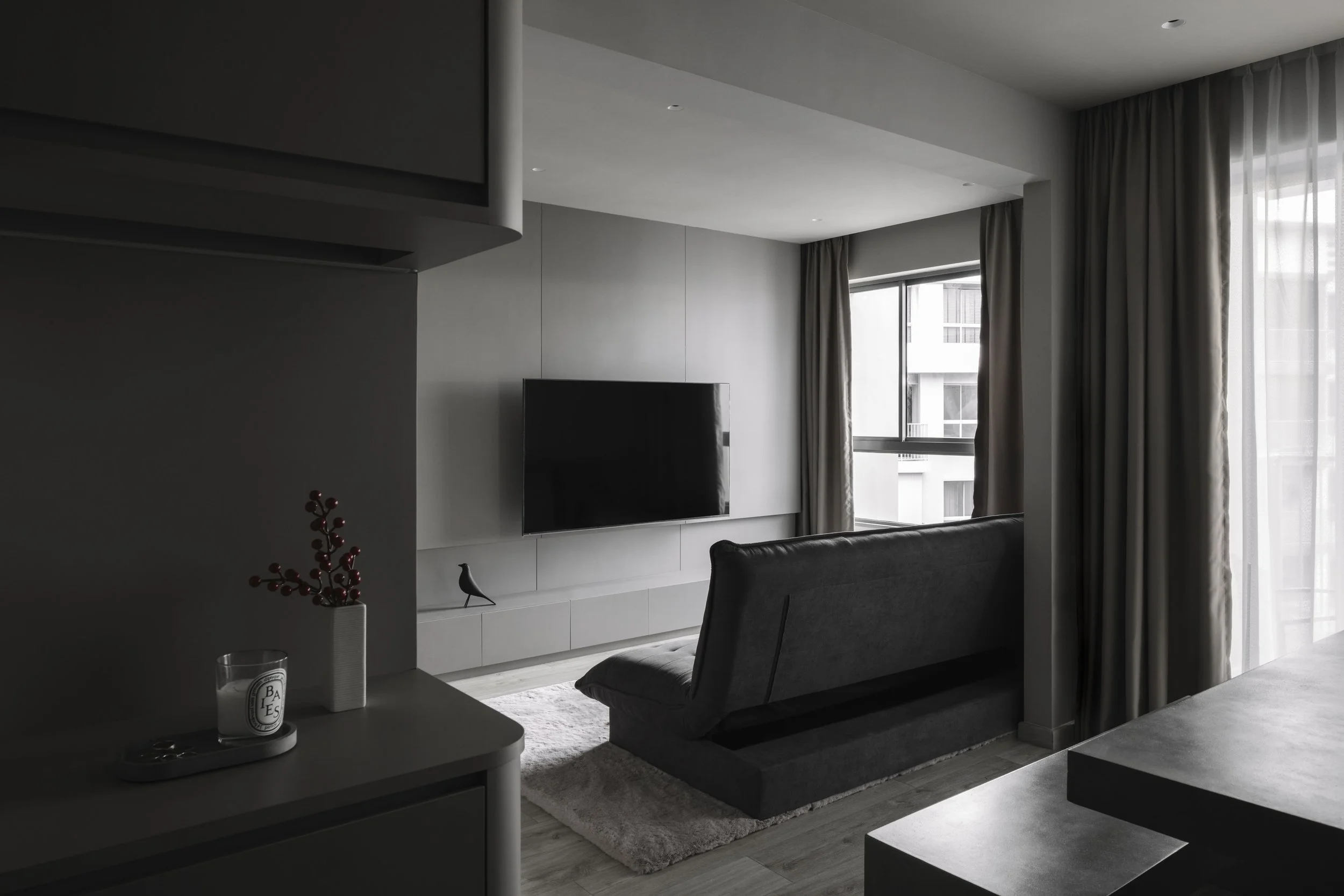 Monochromatic DBSS living room interior at YC138 with minimalist TV wall, dark sofa and full-height curtains designed by Lite Design Collaborative.