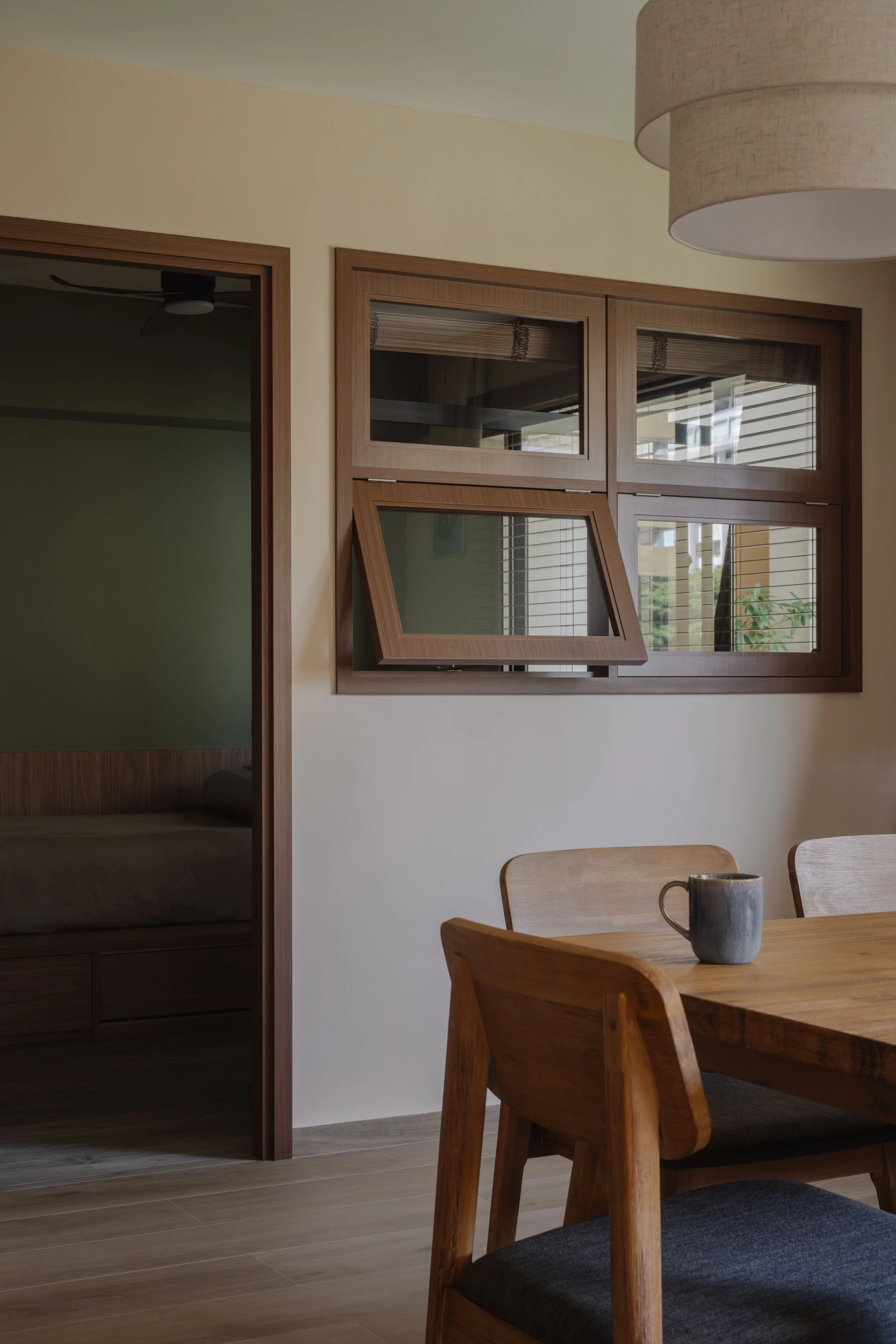 Warm wooden dining corner in a modern Singapore home, featuring crafted timber windows and a serene bedroom entry in a minimalist interior design.