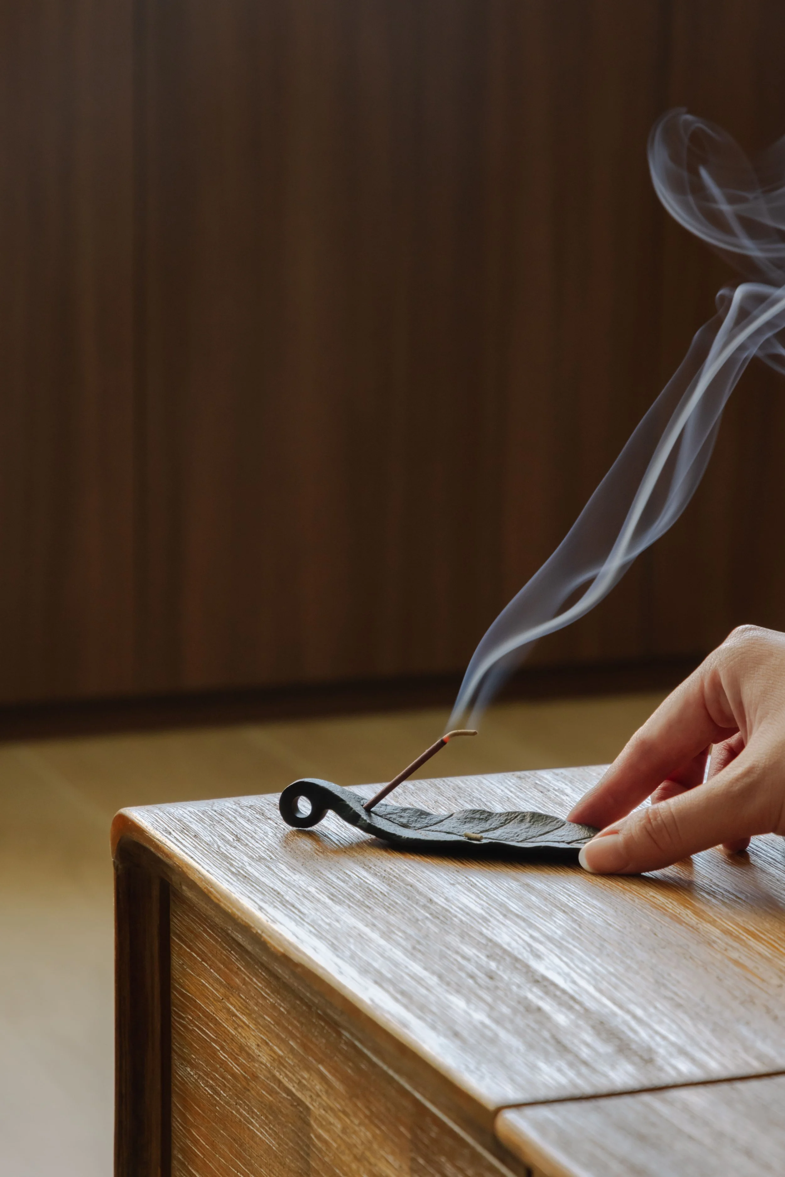 Close-up of incense burning on a wooden table in a modern Singapore living room, showcasing warm natural textures and calming interior details.