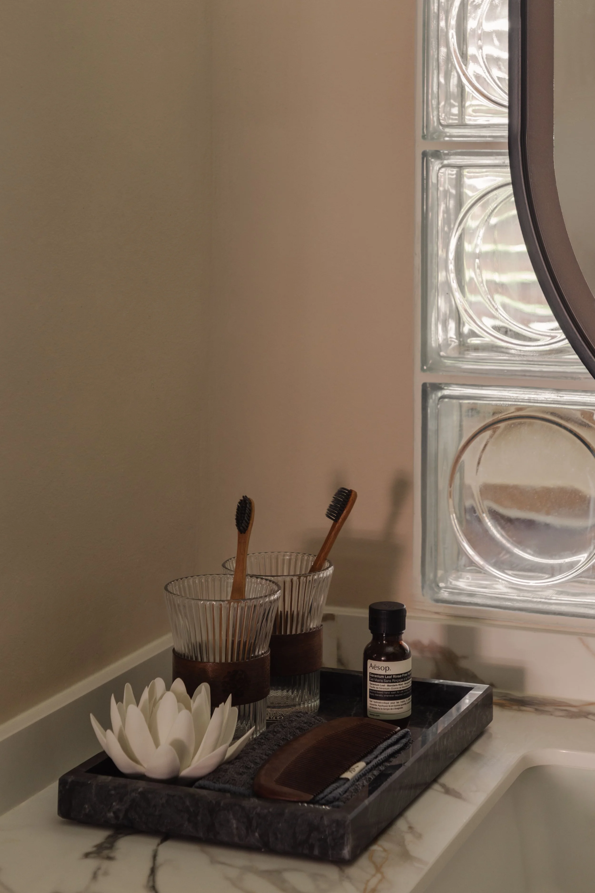 lose-up of a minimalist vanity setup with marble countertop, glass block wall and wooden toothbrushes in a modern Singapore home.