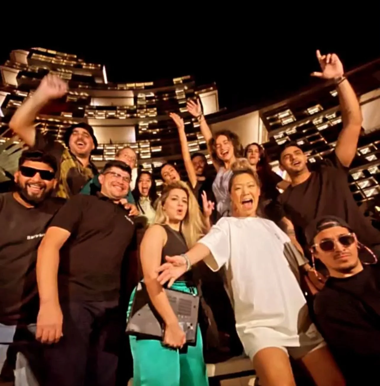Group of people posing happily in front of a modern building at night.