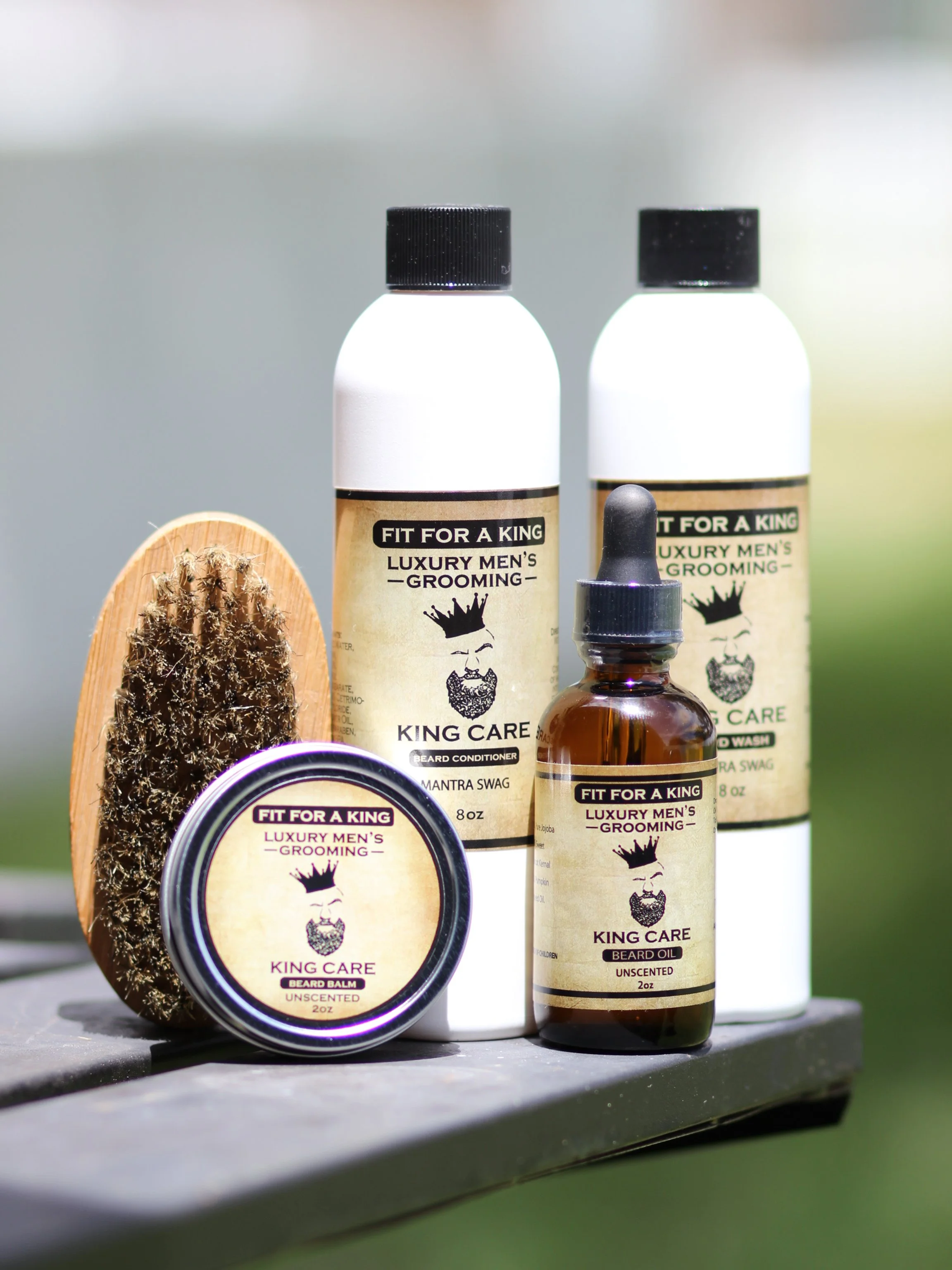 A collection of luxury men's grooming products including beard conditioning, beard balm, beard oil, and beard wash on a wooden surface with a brush and natural background.