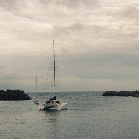 A sailboat floating in a harbor between two rocky breakwaters under cloudy sky.