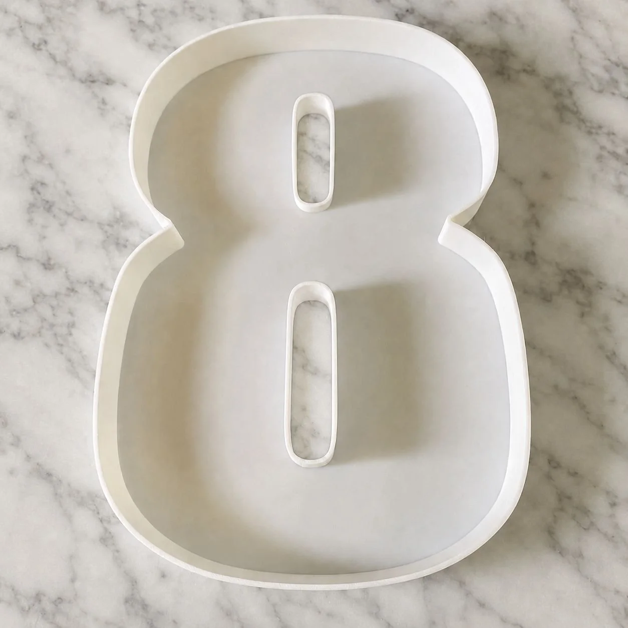 White plastic container with a fillable number 8 shape, placed on a marble surface.