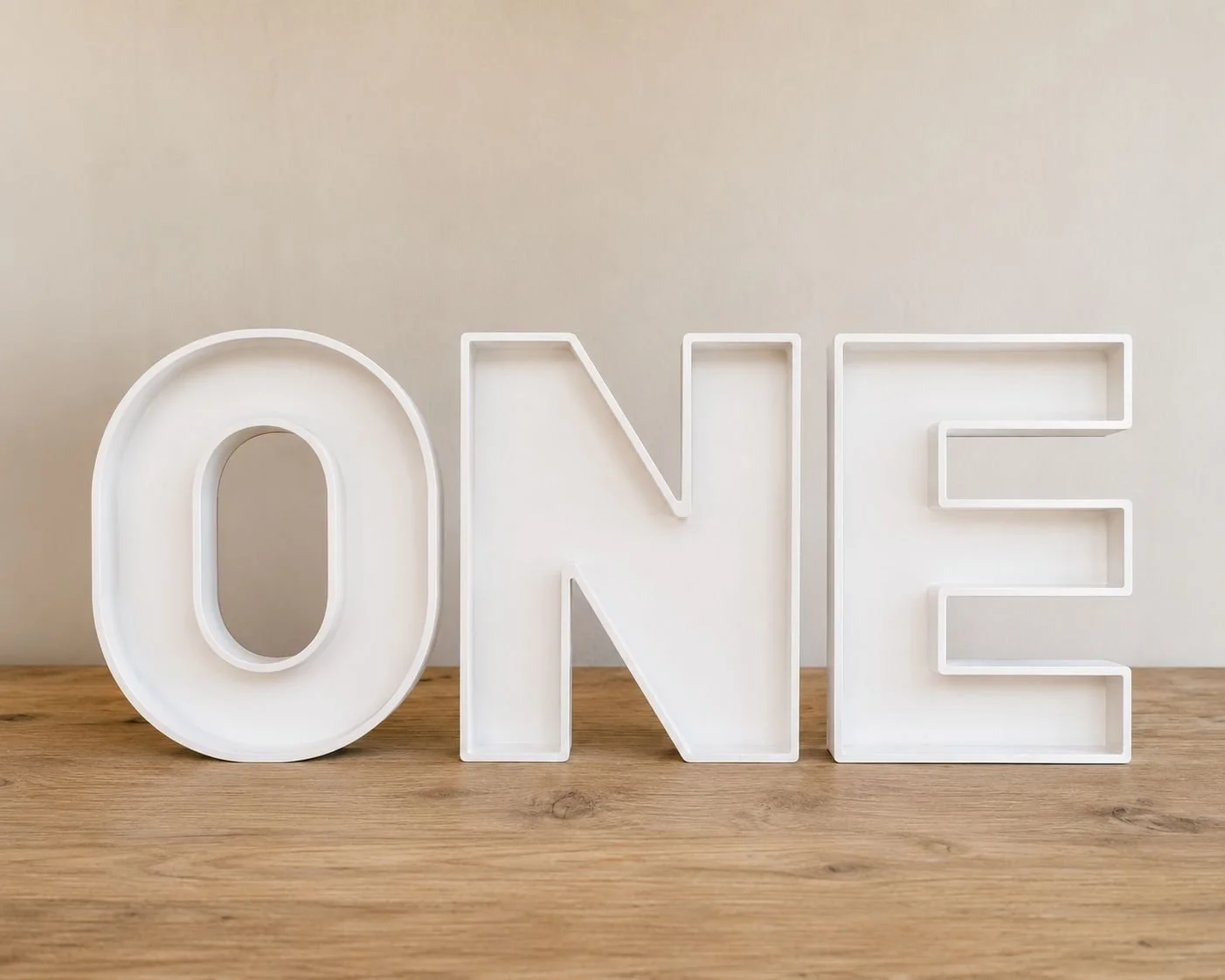 White decorative Charcuterie letters spelling 'ONE' on a wooden surface against a neutral background.