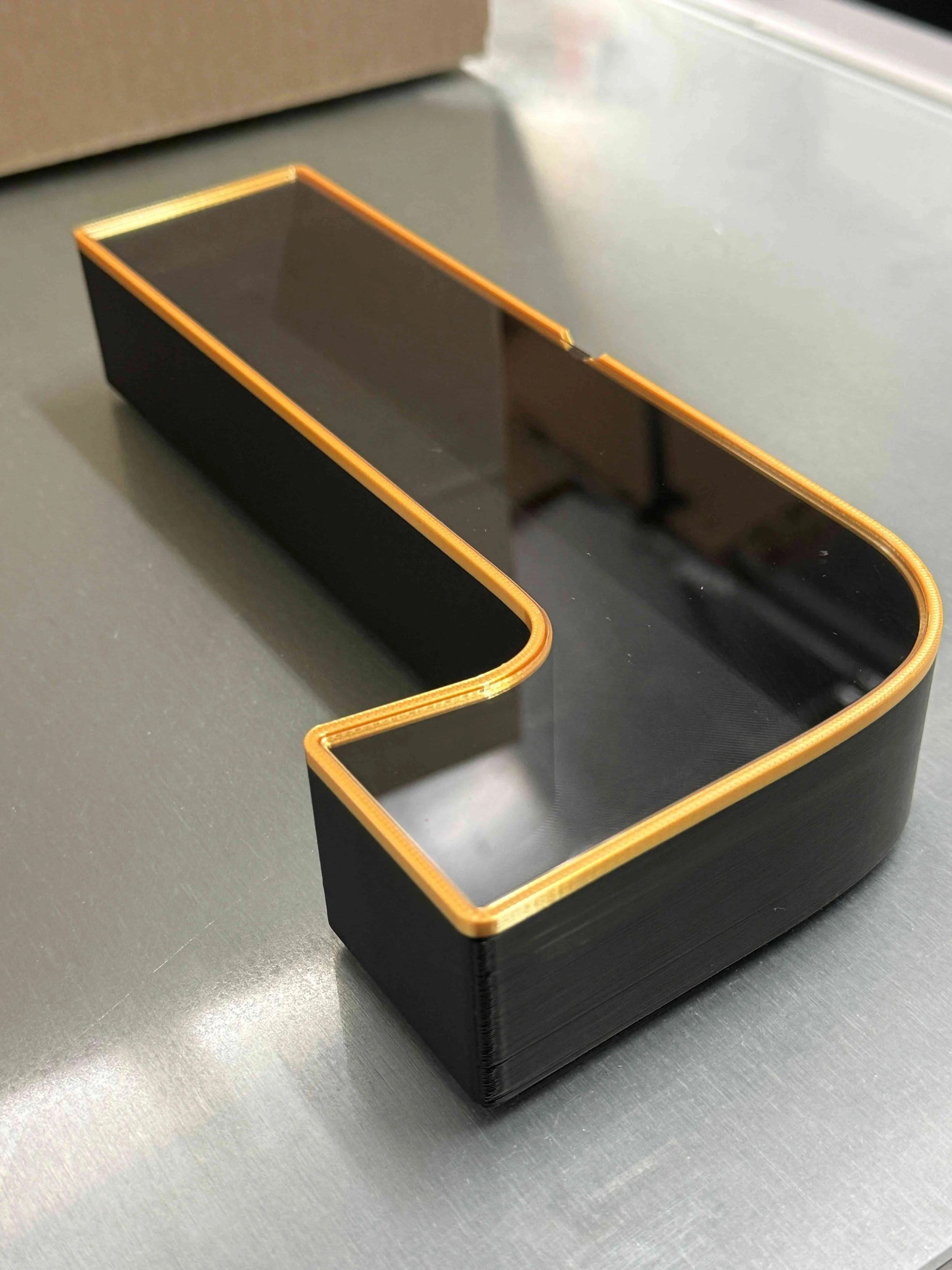 Black rectangular letter box with gold trim on a glass surface.