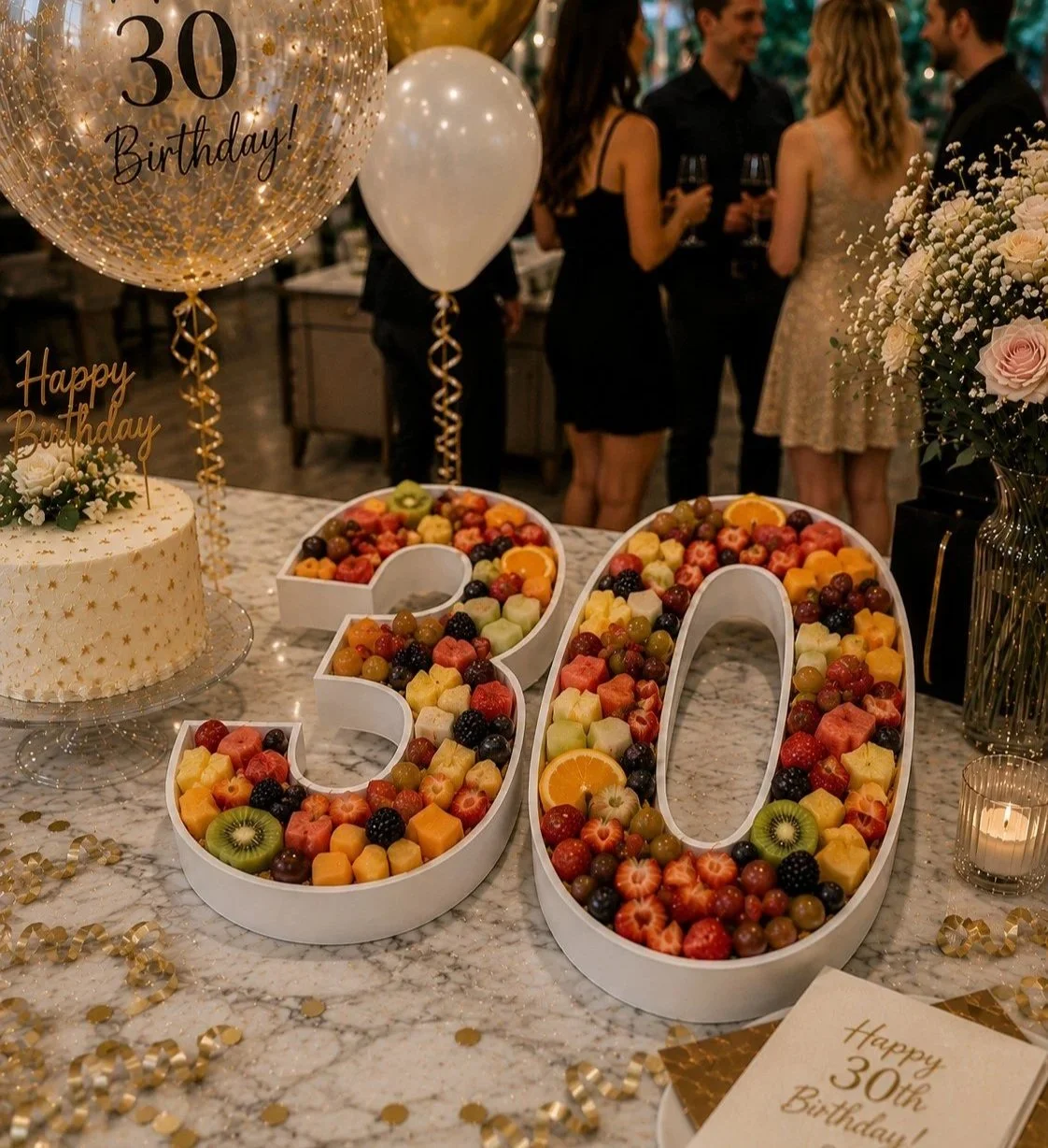 Fillable number platters 30 for a birthday party celebration with a decorated table featuring a fruit arrangement. There are balloons, and guests chatting with drinks in hand.