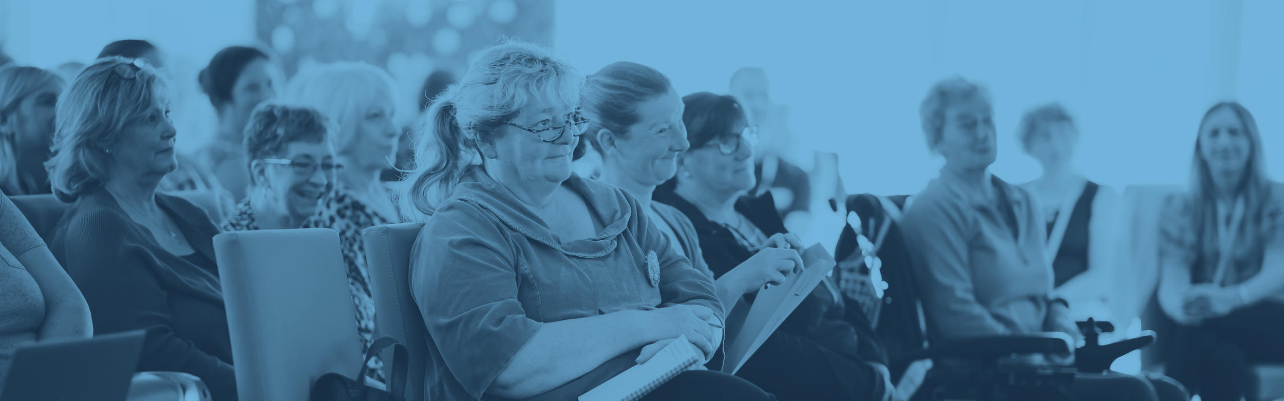 A crowd of people sitting and watching a presentation. Many are smiling and laughing.