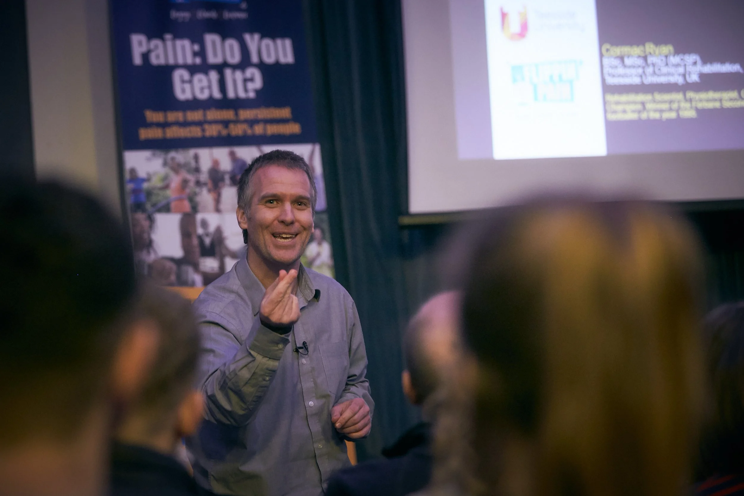 A photograph of speaker Cormac speaking to an audience in front of a Flippin' Pain banner.