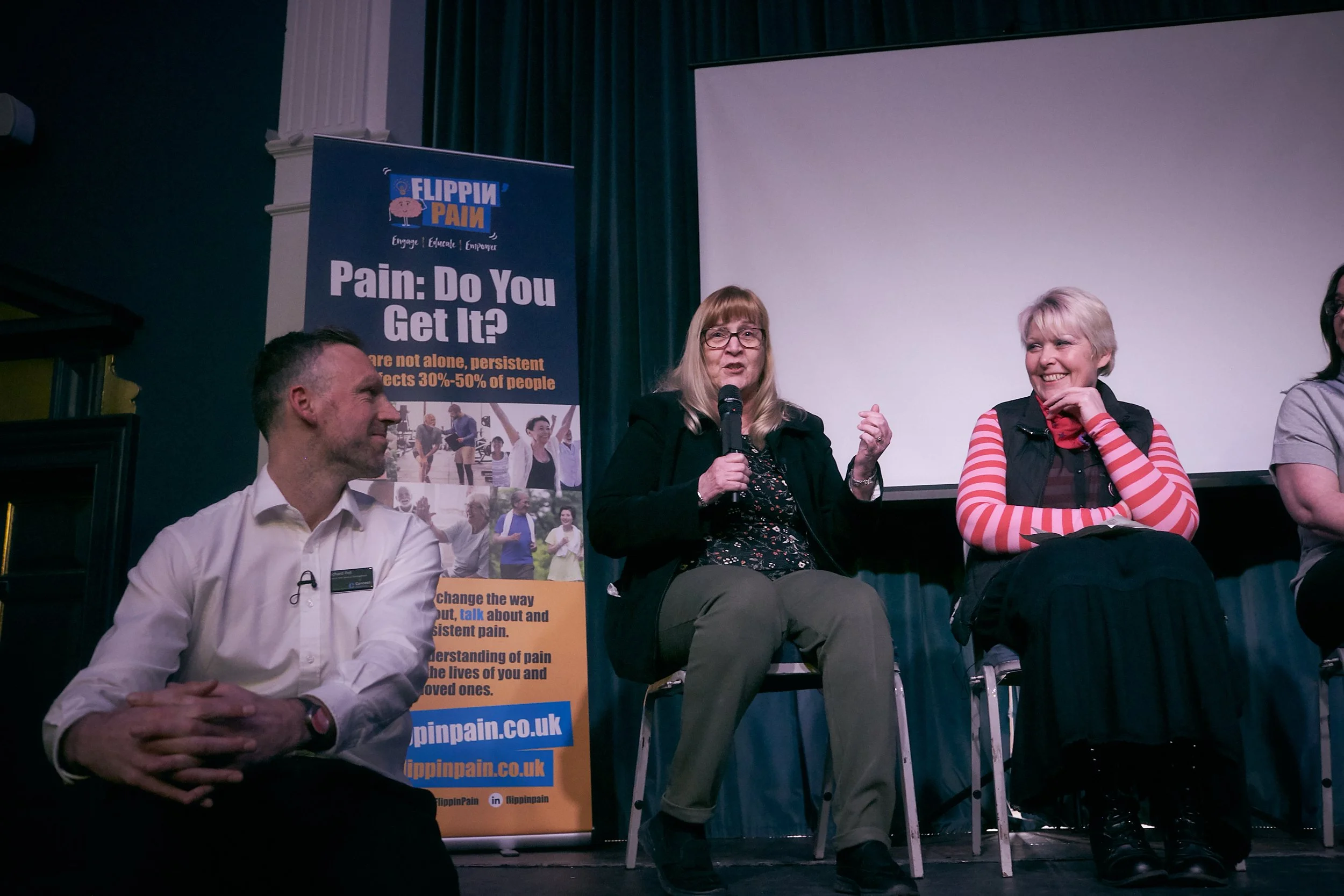 Lived experience contributor Carolyn speaking into a microphone at an event. People are smiling around her.