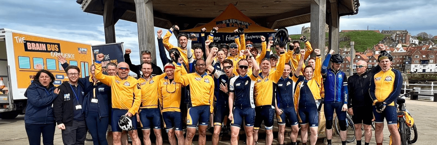 A photograph of everyone who was involved in the Flippin' Pain Outreach Tour. Most are in cycling gear and have their hands in the air.