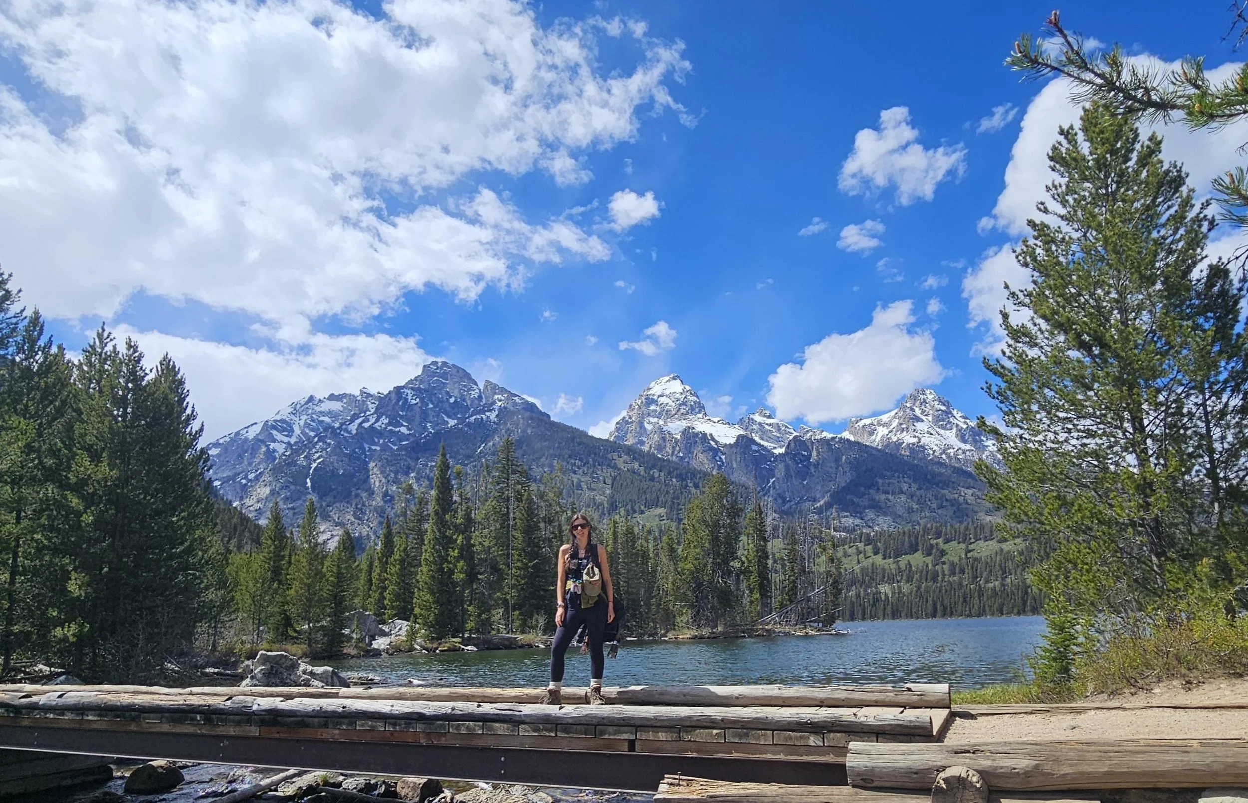 A lady standing on a bridge over a lake with mountains in the bakground