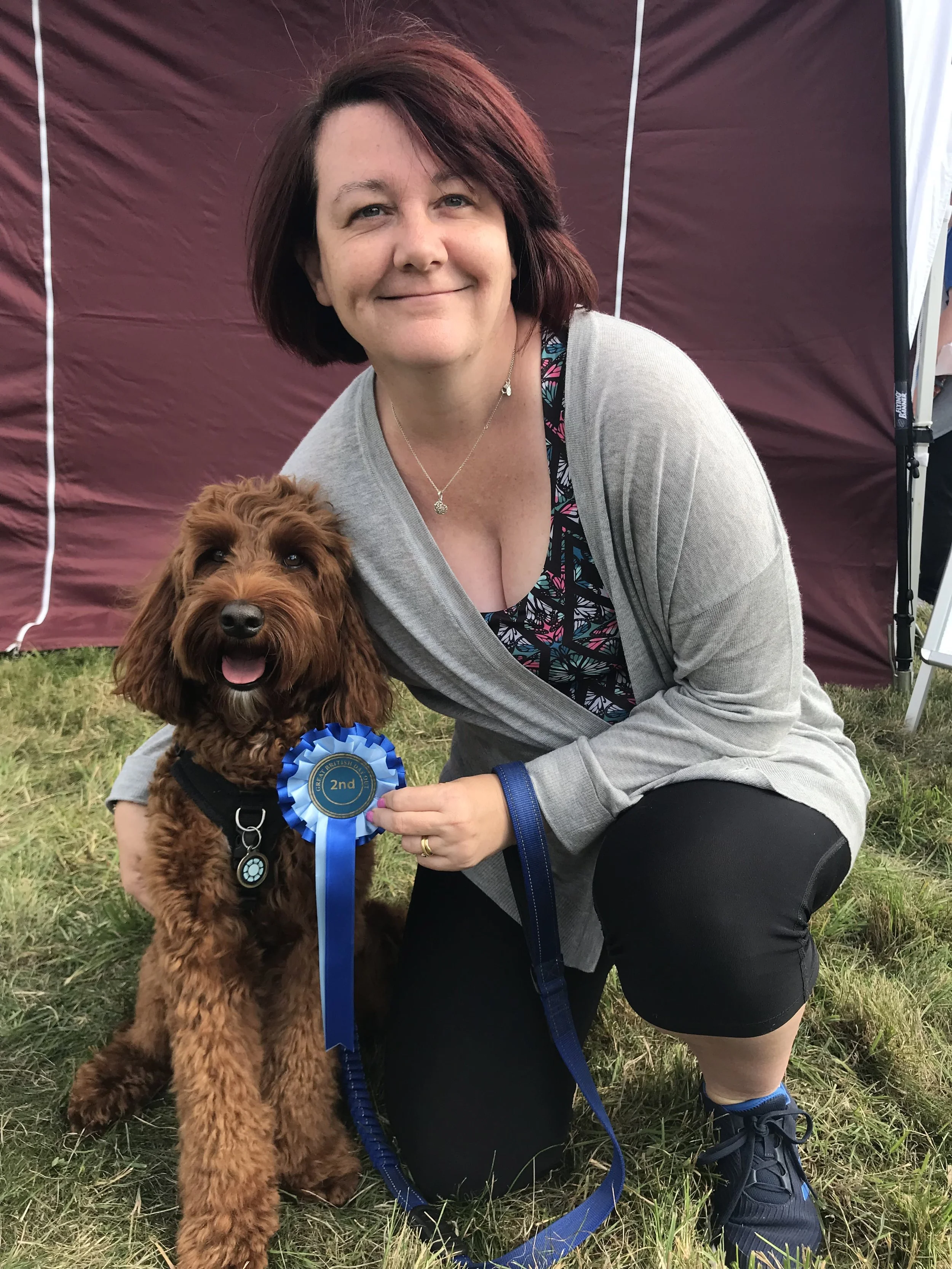 Steph holding her dog and a rosette, smiling.
