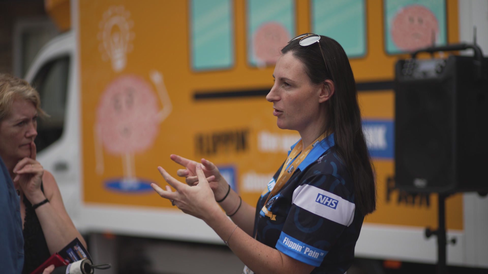 An image of Flippin' Pain team member Julia speaking in front of a Flippin' Pain branded van..