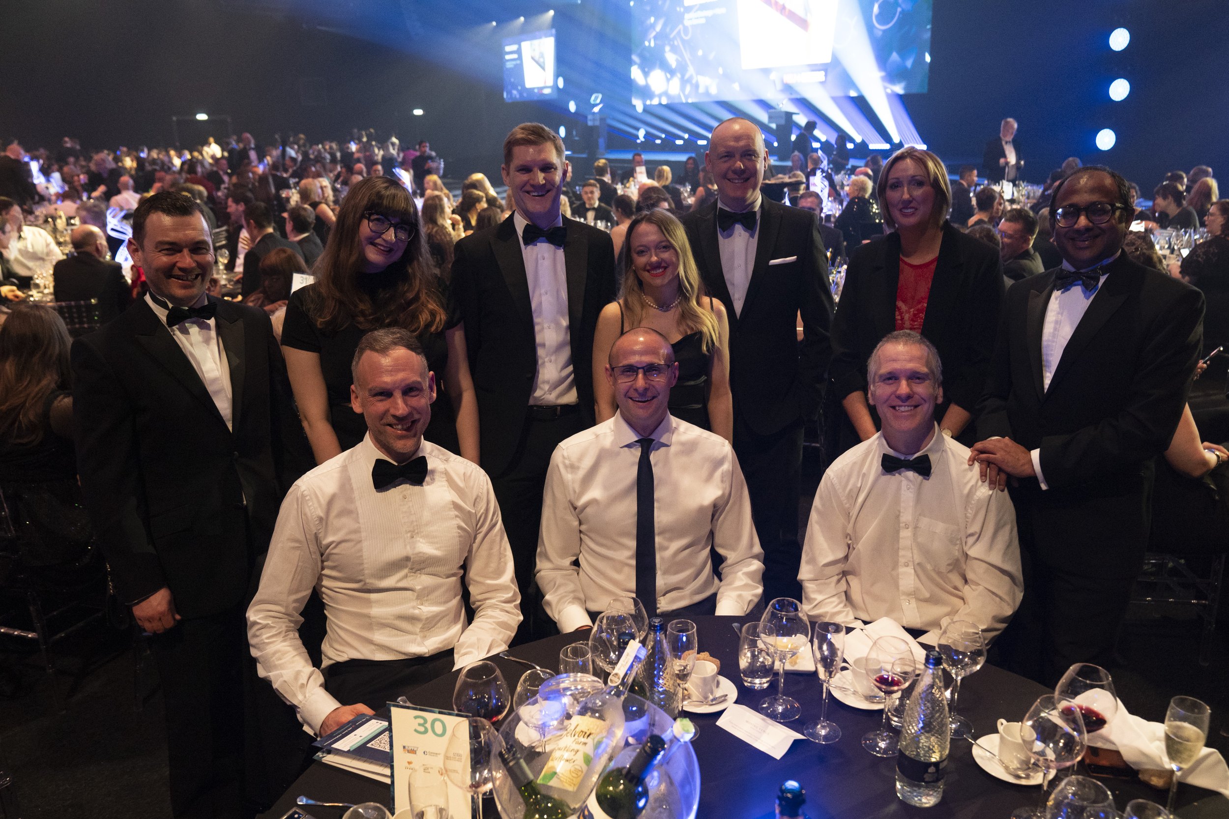 A photograph of Flippin' Pain team members and their partners standing around  a dining  table, smiling.
