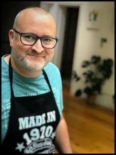 Ian wearing a cooking apron, smiling.