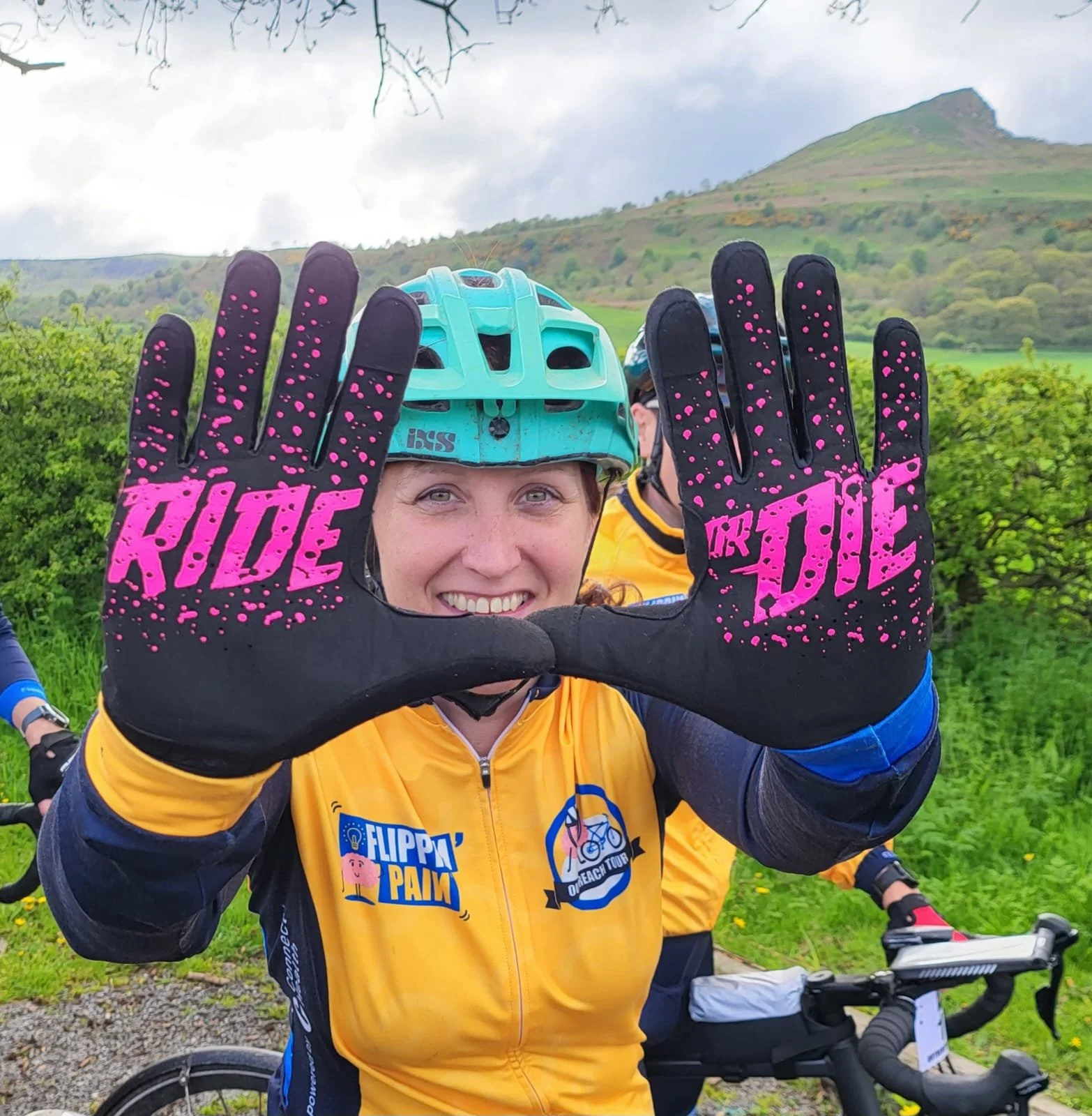 Liz in a Flippin' Pain hoodie, holding up her hands. Her gloves say 'ride or die'.
