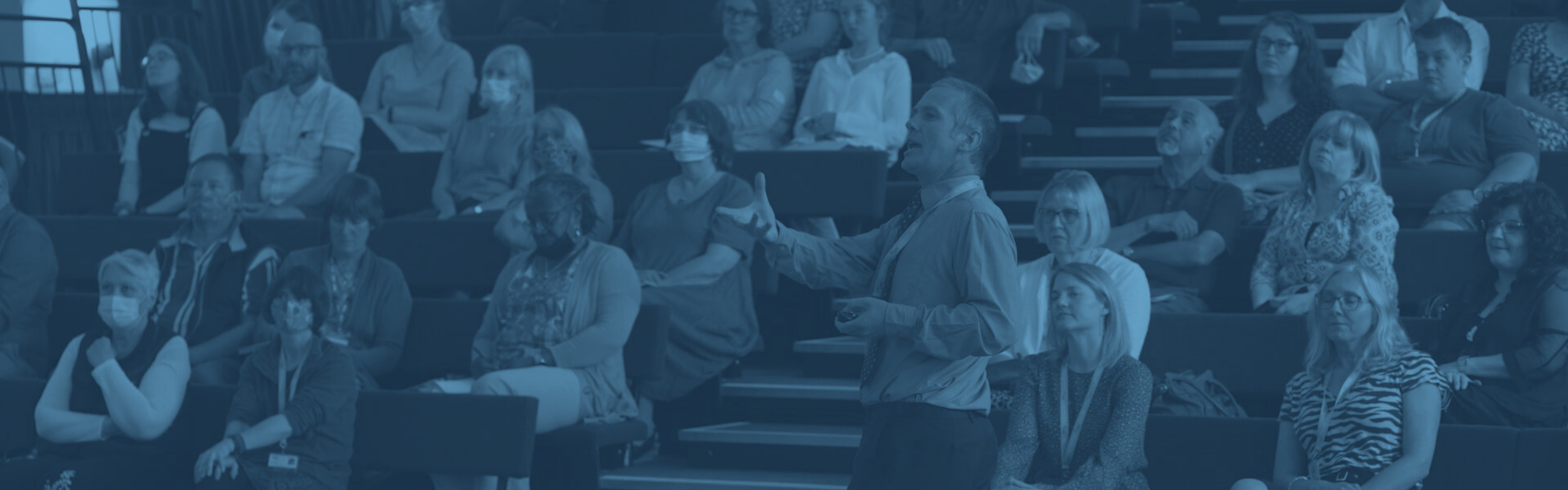 A speaker presenting with his back to a lecture theatre of people.