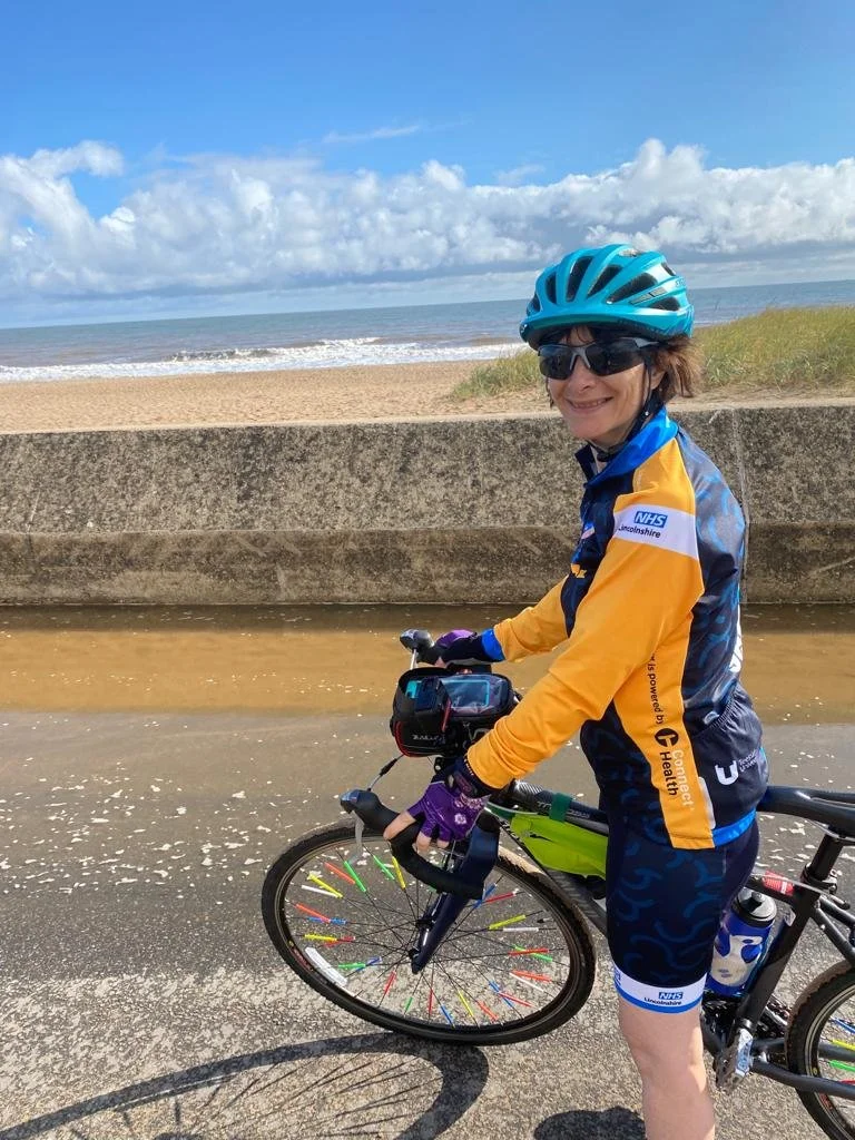 Niki on a path next to the beach, standing next to her bike and smiling.