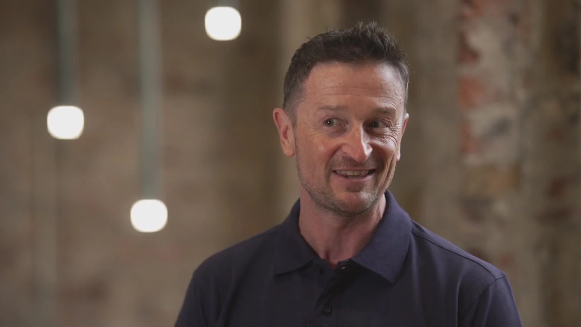 An image of lived experience participant Lee standing in front of a brick wall, smiling.