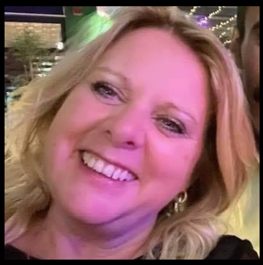 Close-up of a smiling woman with blonde, wavy hair and earrings in a lively, decorated setting with string lights.