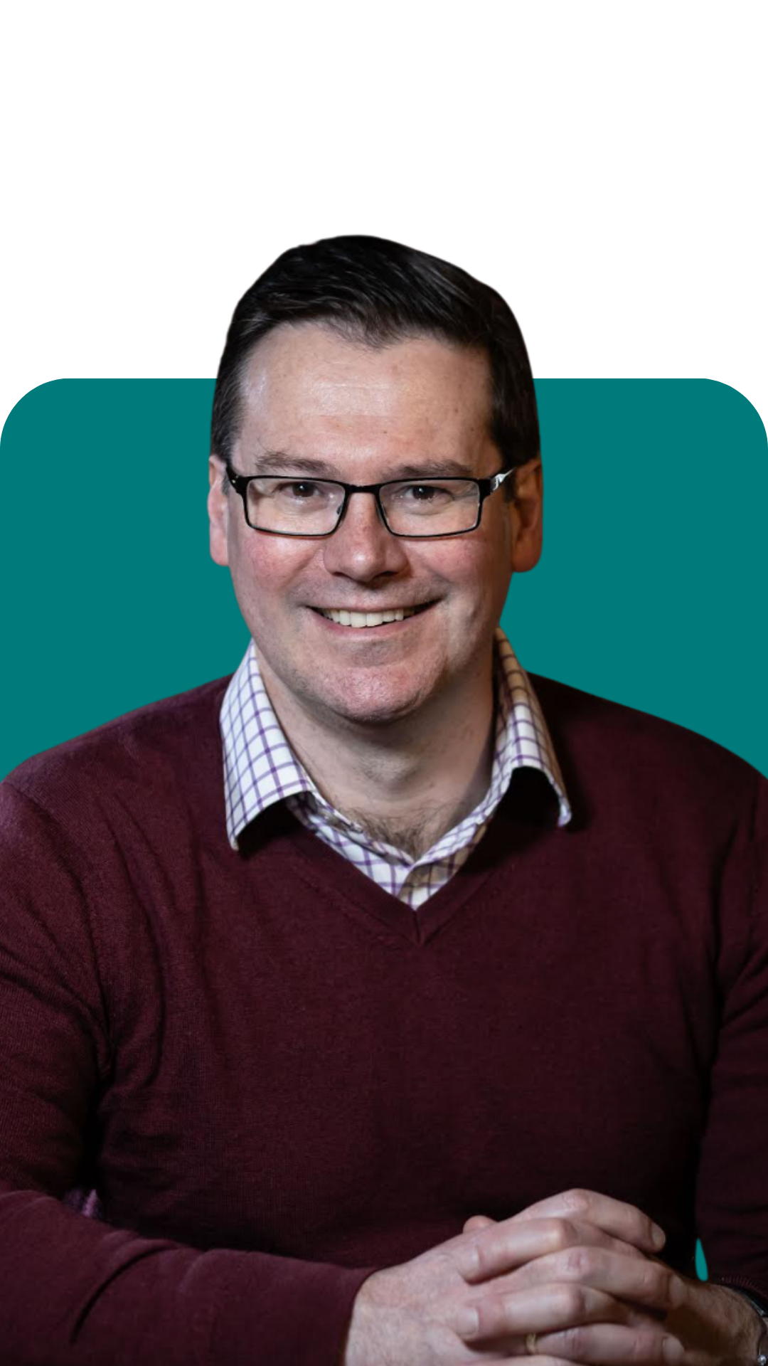 Portrait of a smiling man with glasses, wearing a maroon sweater and checkered shirt, seated with hands clasped, against a teal and black background.