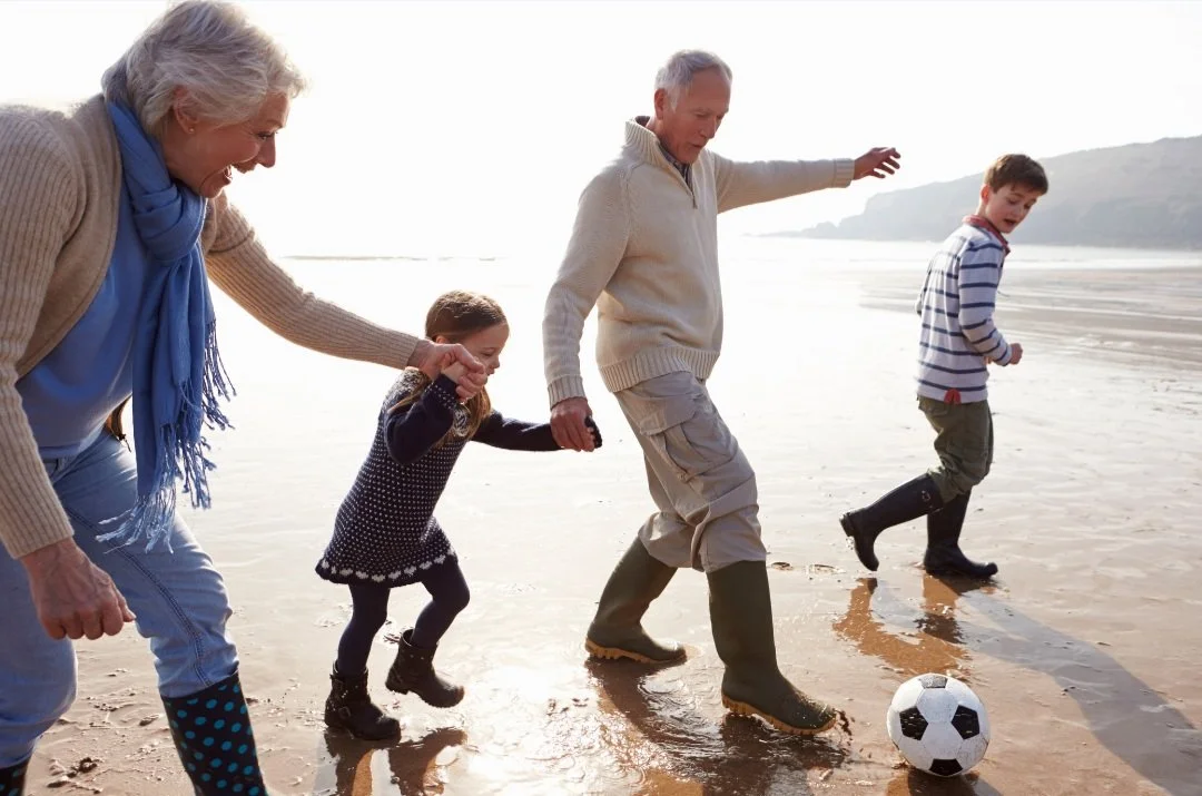 Grandparents and children playing soccer on the beach with a ball near the water