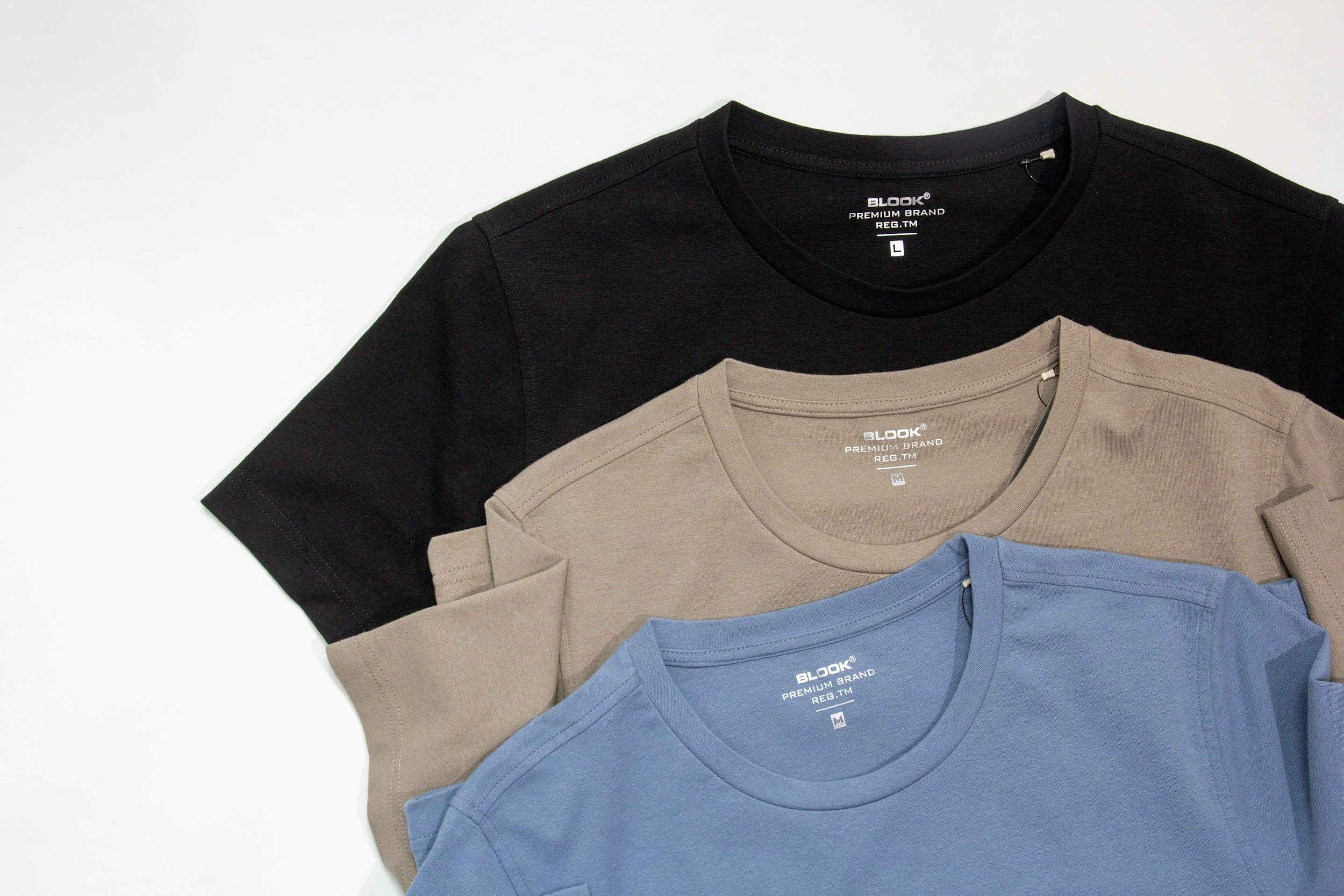 Three folded T-shirts in black, beige, and blue laid out on a white background.