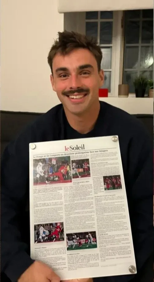 A smiling young football player holding his Le Soleil game story, printed on clear acrylic
