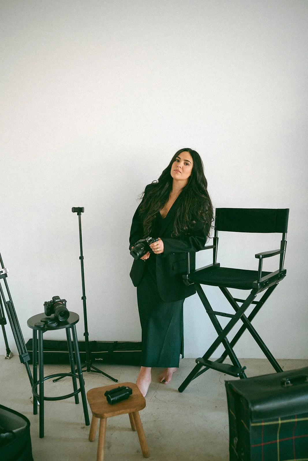 A woman in black outfit holding a camera in a photography studio with equipment around her for her New Jersey wedding videography business.