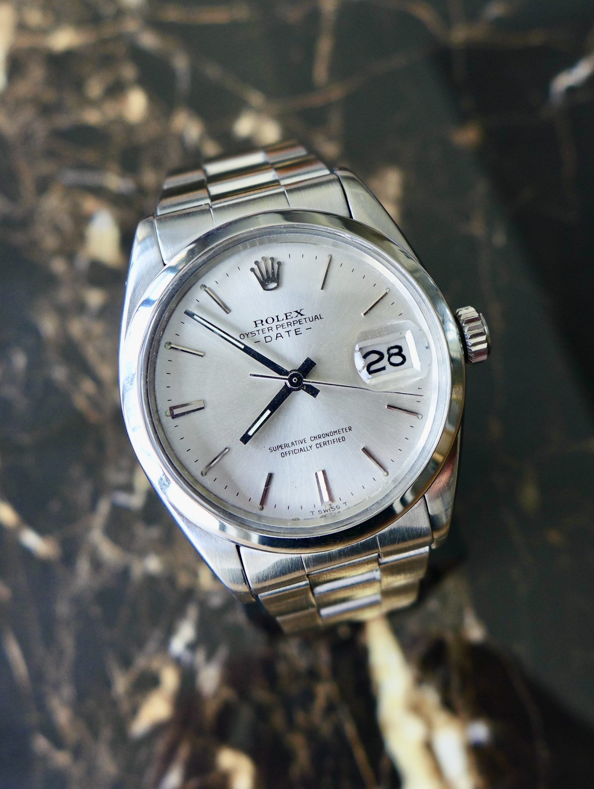 Silver Rolex Oyster Perpetual Date watch on a dark marble background.
