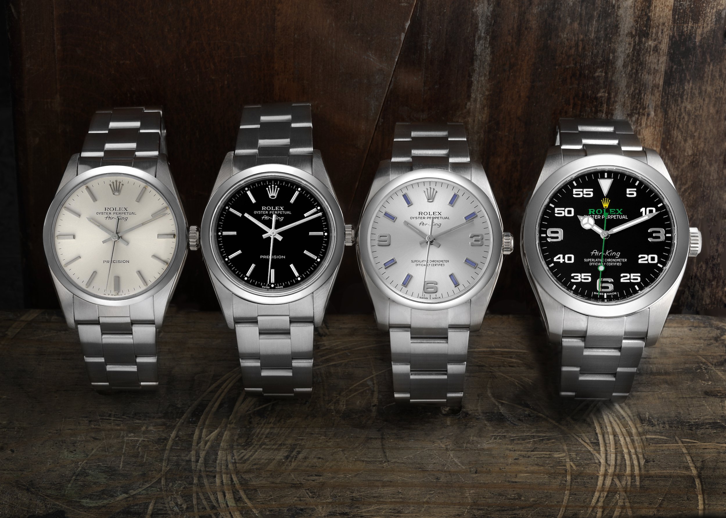 Four Rolex Air-King watches with stainless steel bracelets and different dial colors, displayed side by side on a wooden surface.