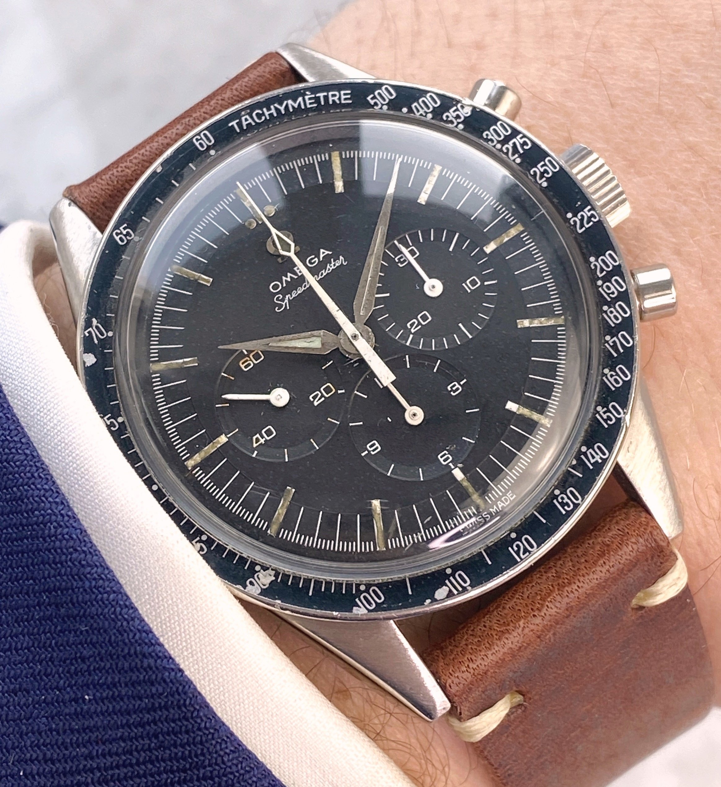 A vintage Omega Speedmaster watch with a black dial and tachymeter bezel, featuring three subdials and a brown leather strap.