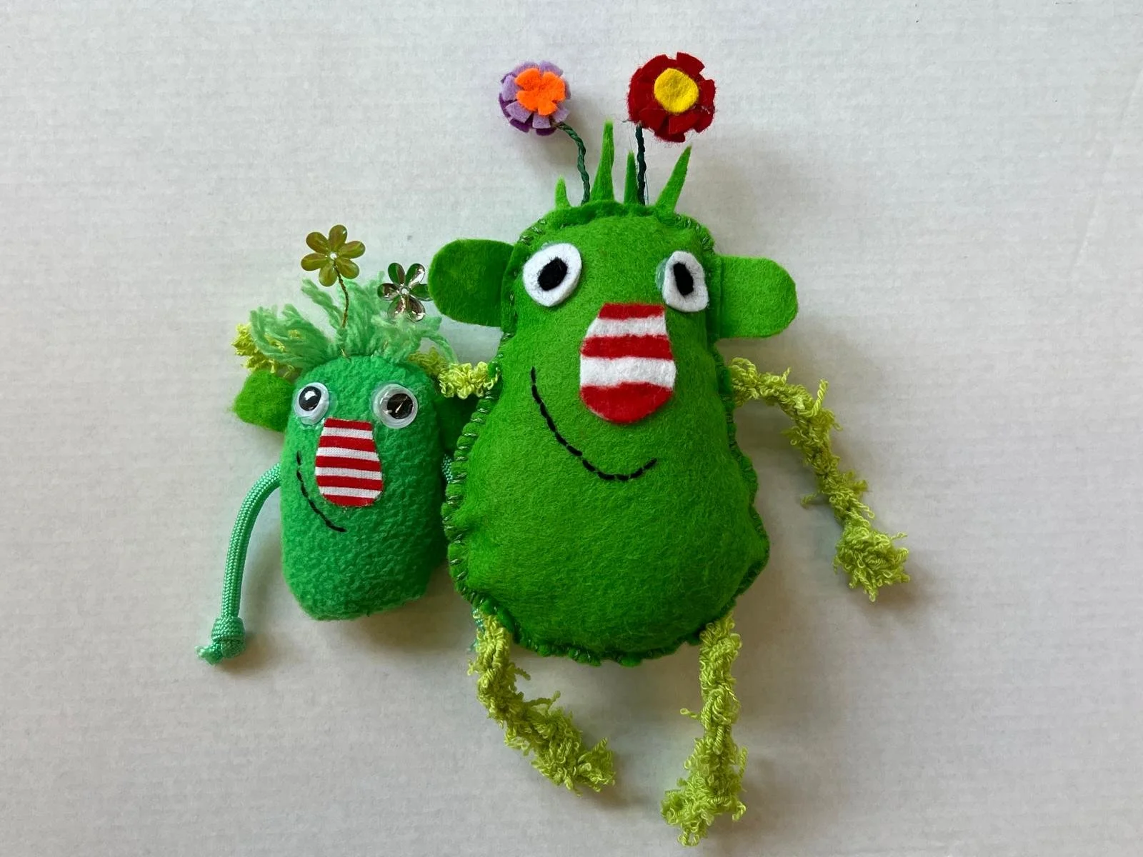 Zwei grüne Stoffmonster mit grossen Augen und gestickten Armen, genäht im textilen Werken