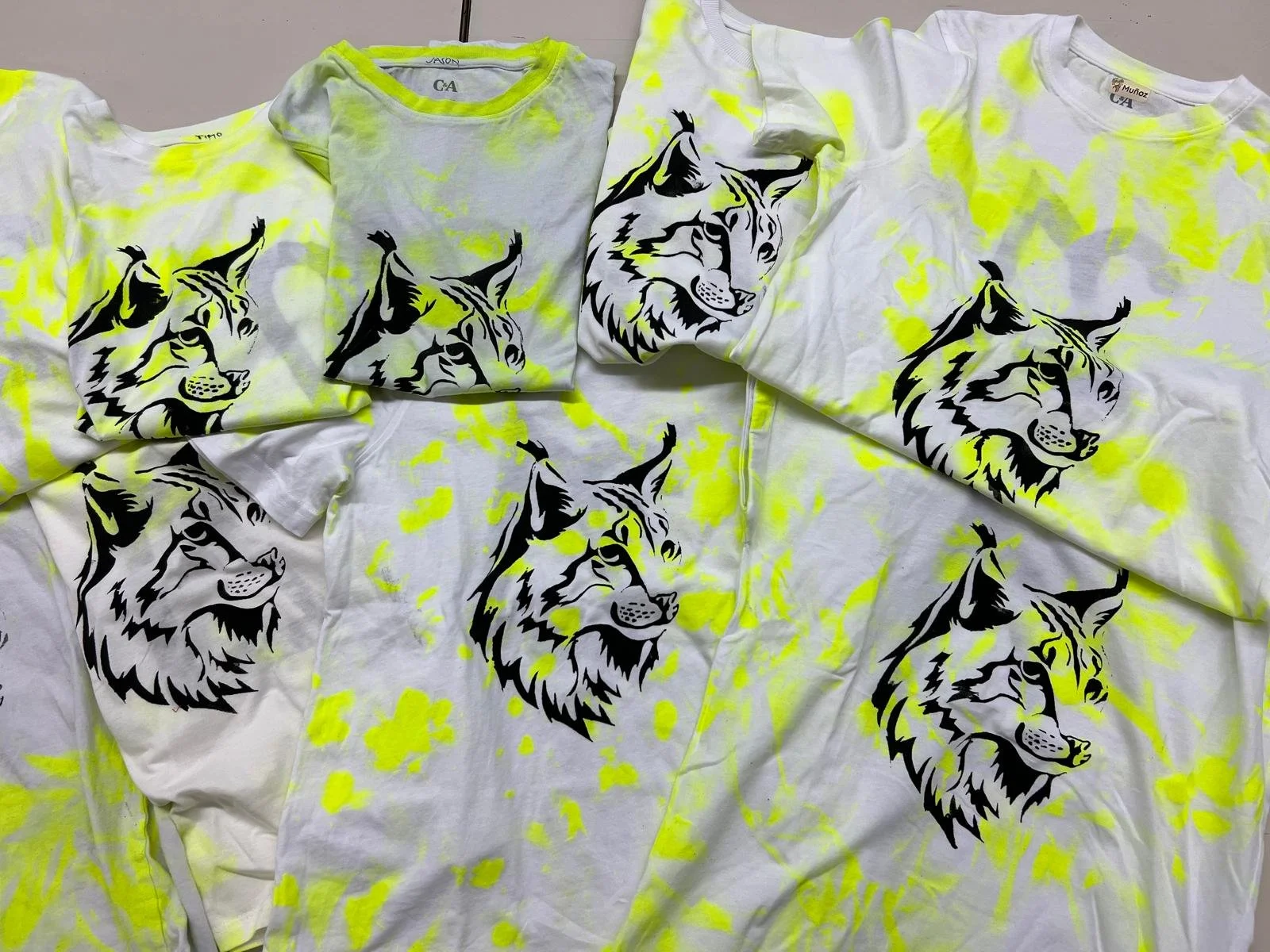 Weisse T-Shirts mit neongelben Farbflecken und aufgedrucktem Wolfskopf