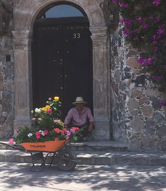 Man sitting in front of stone house with flowers in wheelbarrow