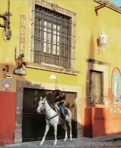 man riding a white horse through Mexican town