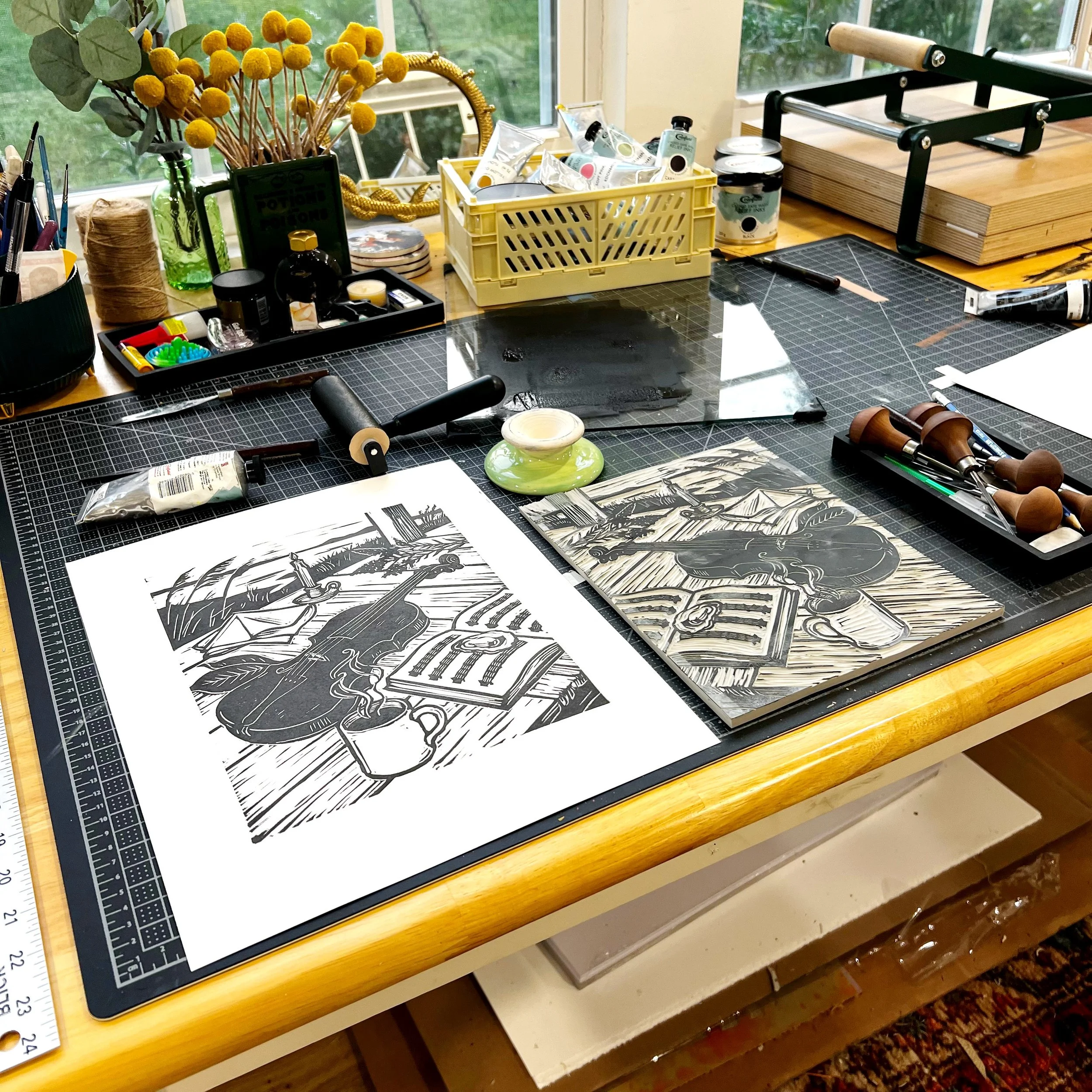 Printmaker's workbench with carved linoleum blocks, carving tools, and a freshly printed black ink relief print.