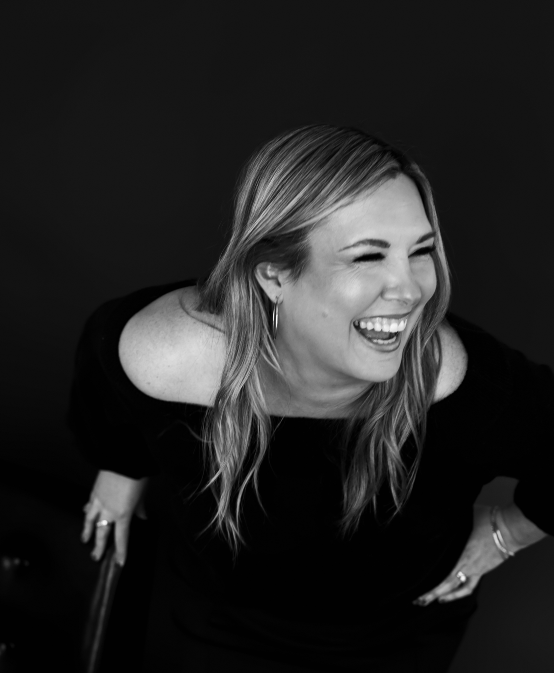 Carissa Hawkins of Home is a Feeling, Indianapolis real estate agent, leaning forward and laughing in a candid black-and-white portrait
