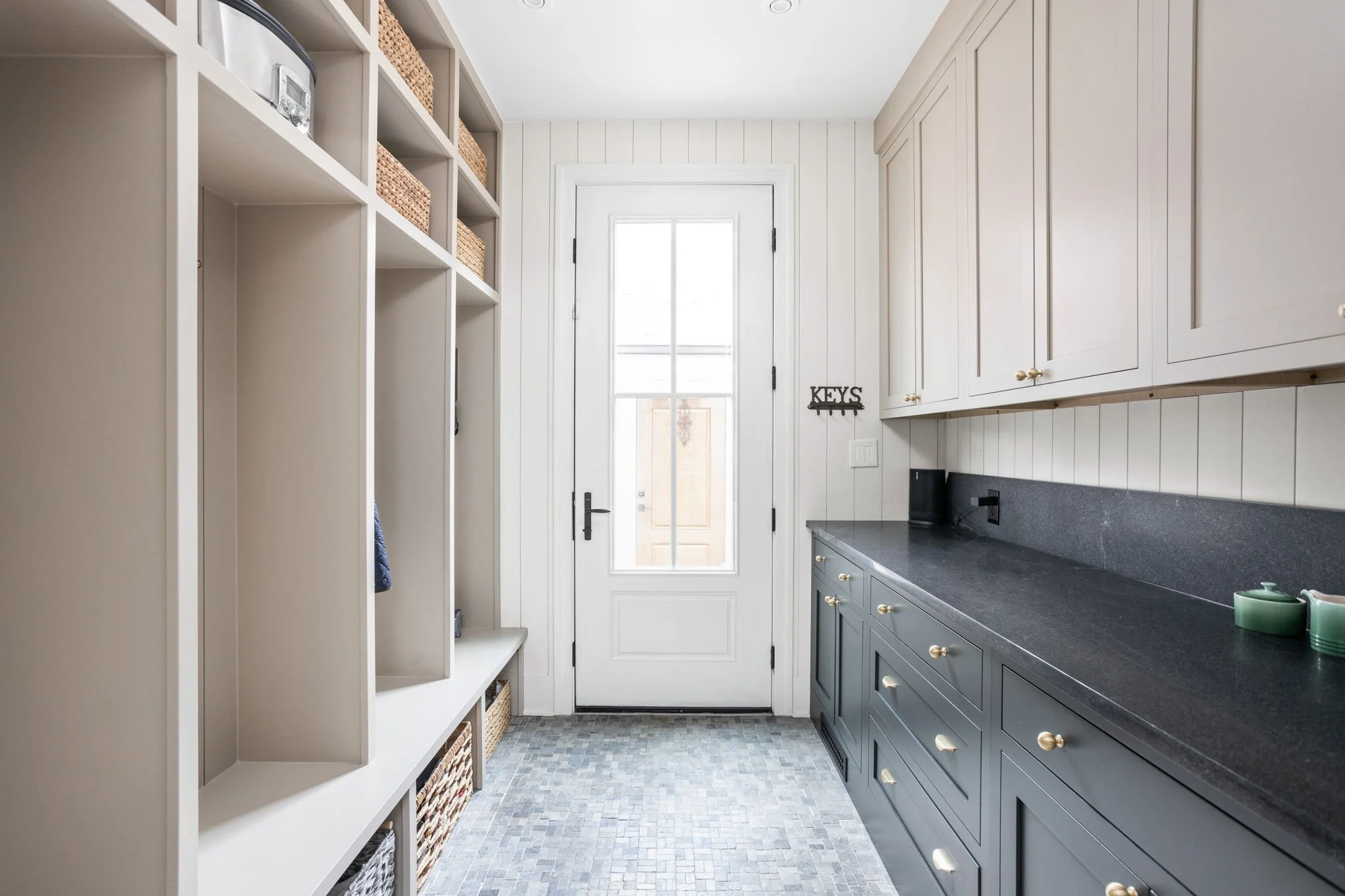 Modern mudroom with built-in shelves, storage baskets, and cabinetry, featuring a glass door and "KEYS" wall hook.
