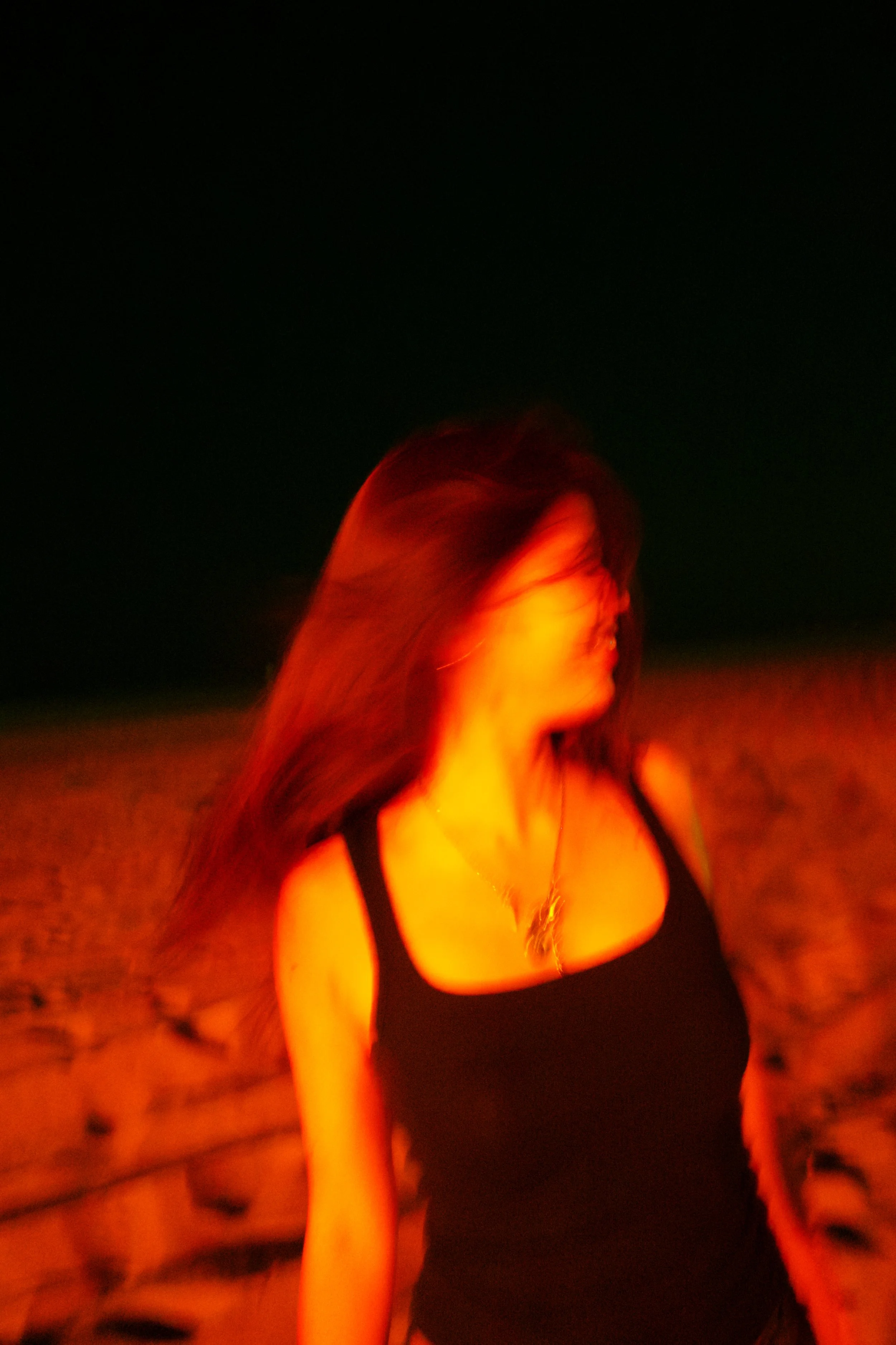A woman with long hair wearing a black top, standing in front of a bright orange and yellow glowing background, with a black night sky above.