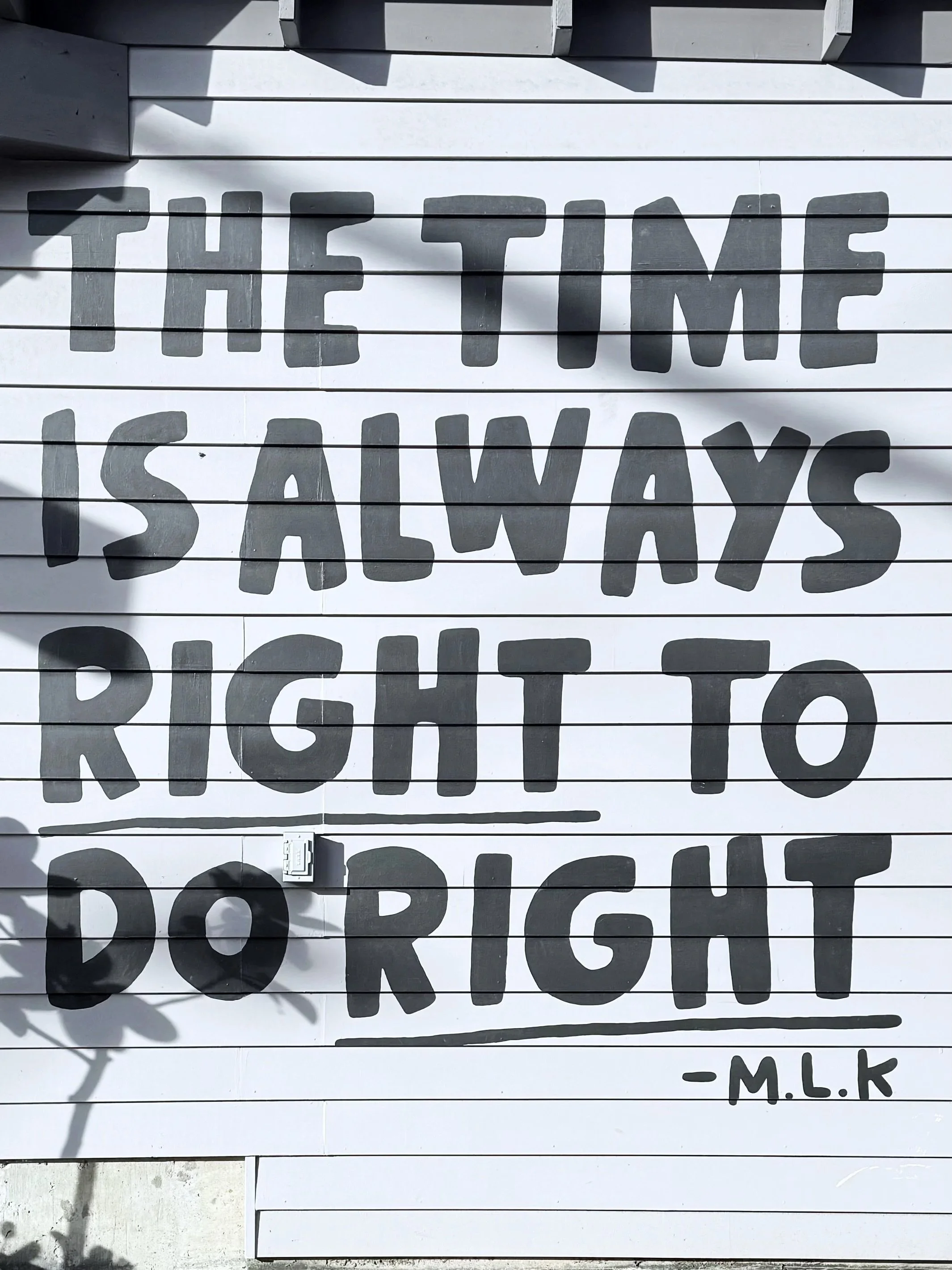 Black letters on a white outdoor wall read: The time is always right to do right" by Martin Luther King Jr.